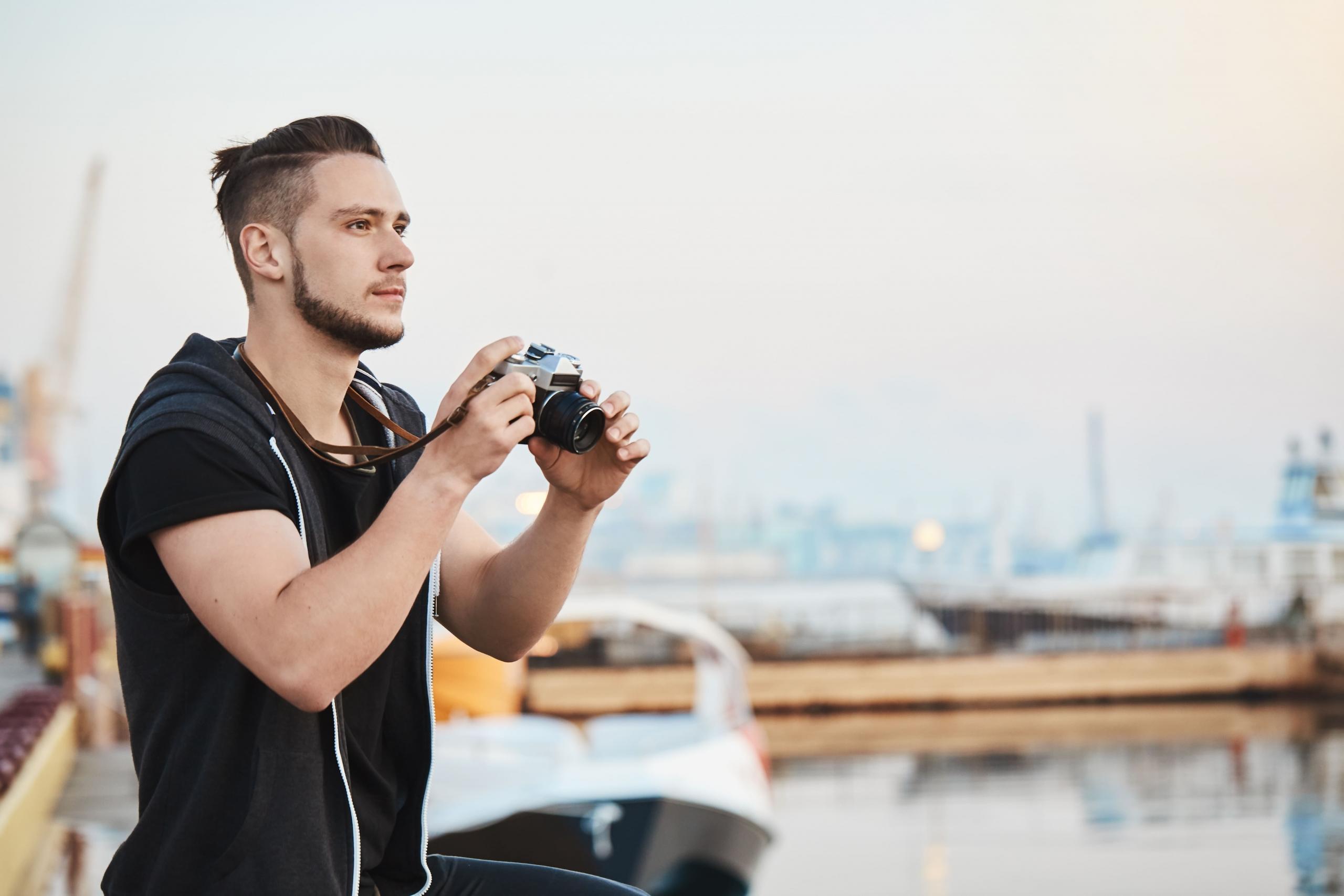 chico con una cámara mirando el horizonte con un fondo de muelle