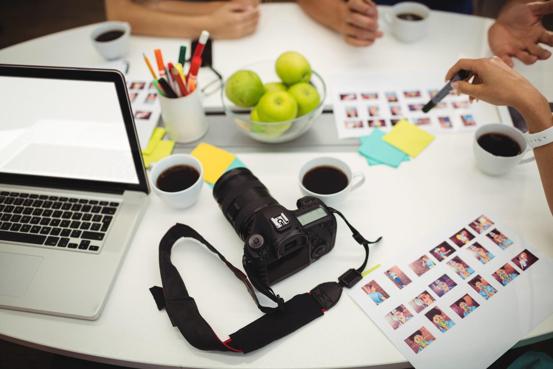 escritorio lleno de cuadros de fotos y cámara sobre la mesa con personas escogiendo imágenes