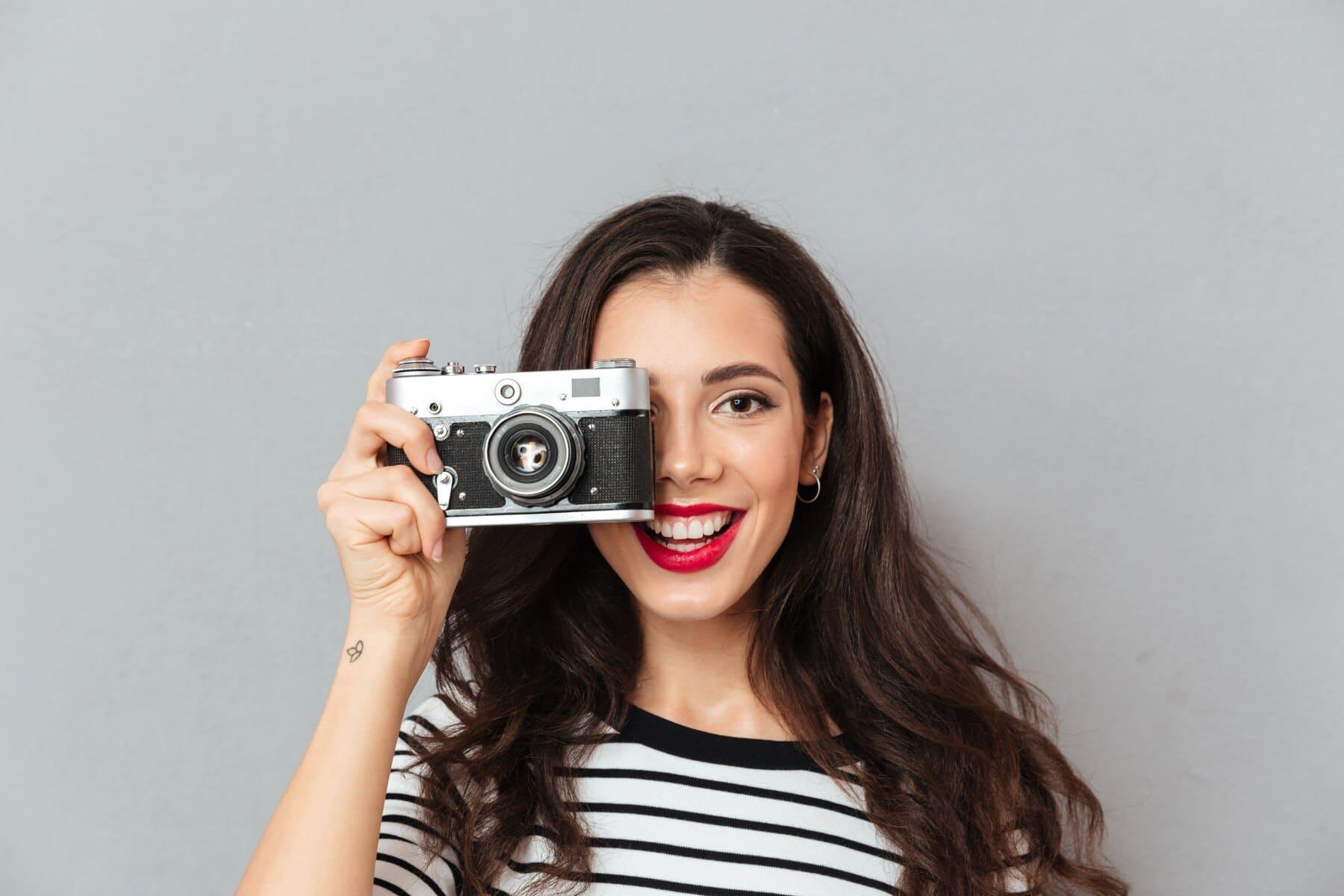 chica sonriente sosteniendo una cámara que tapa parte de su rostro