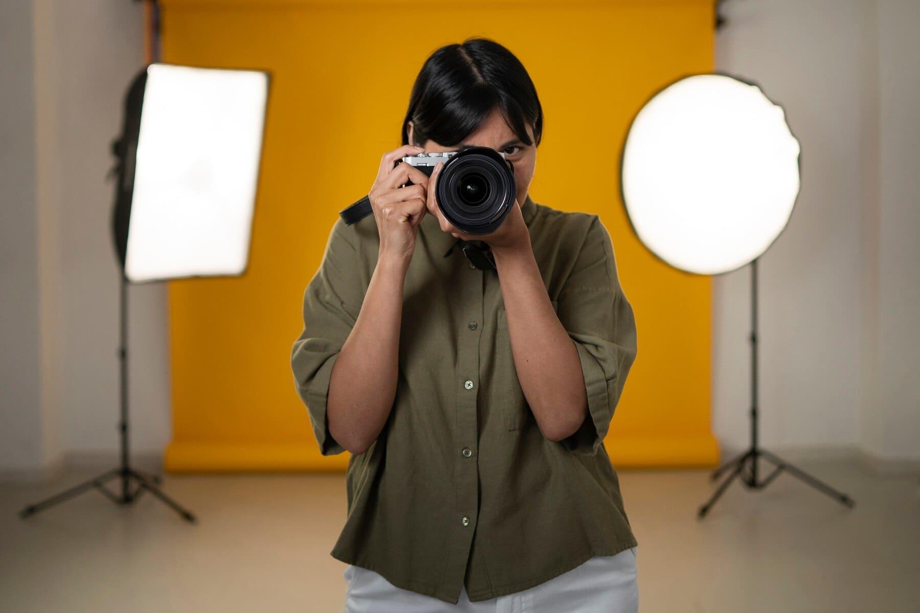 fotógrafa apuntando con la cámara, fondo de estudio amarillo y luces