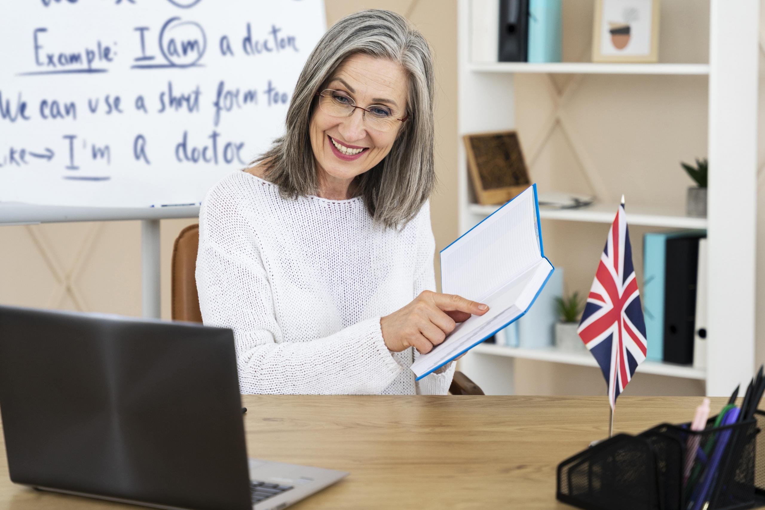 profesora de inglés con un libro en mano mostrándolo a sus alumnos tras una laptop