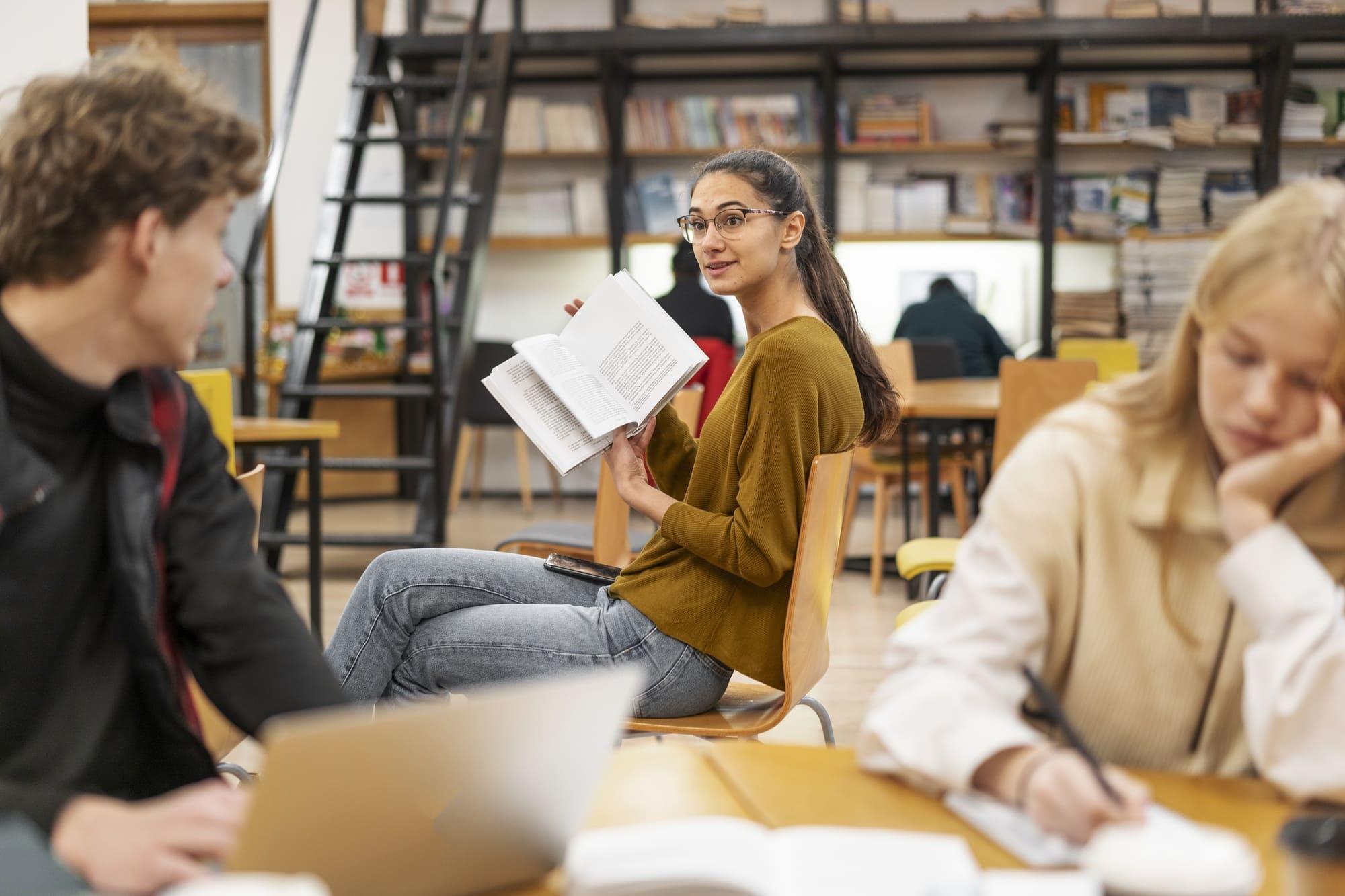 chica sentada mostrando un libro en medio de la biblioteca