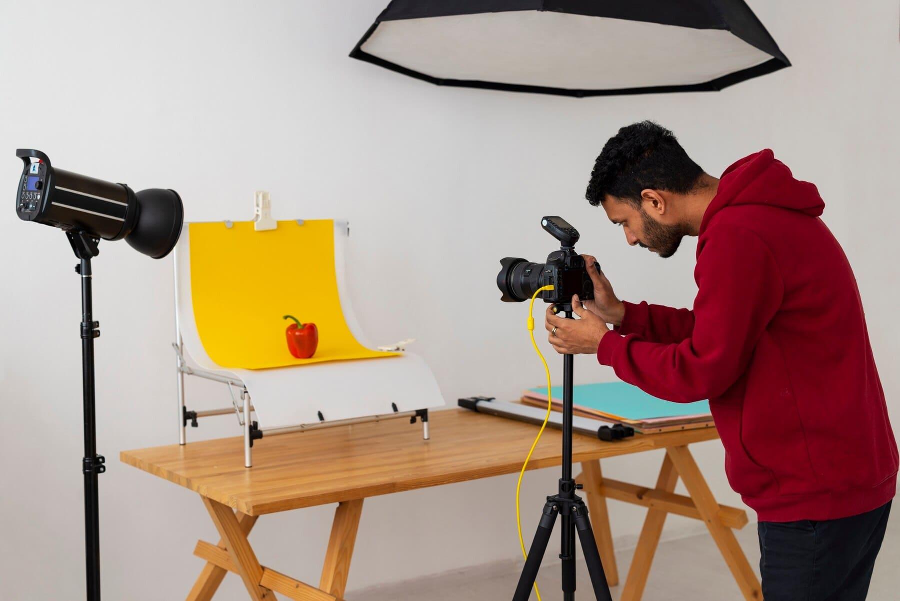 chico en un estudio fotográfico tomándole foto a un pimiento en fondo amarillo