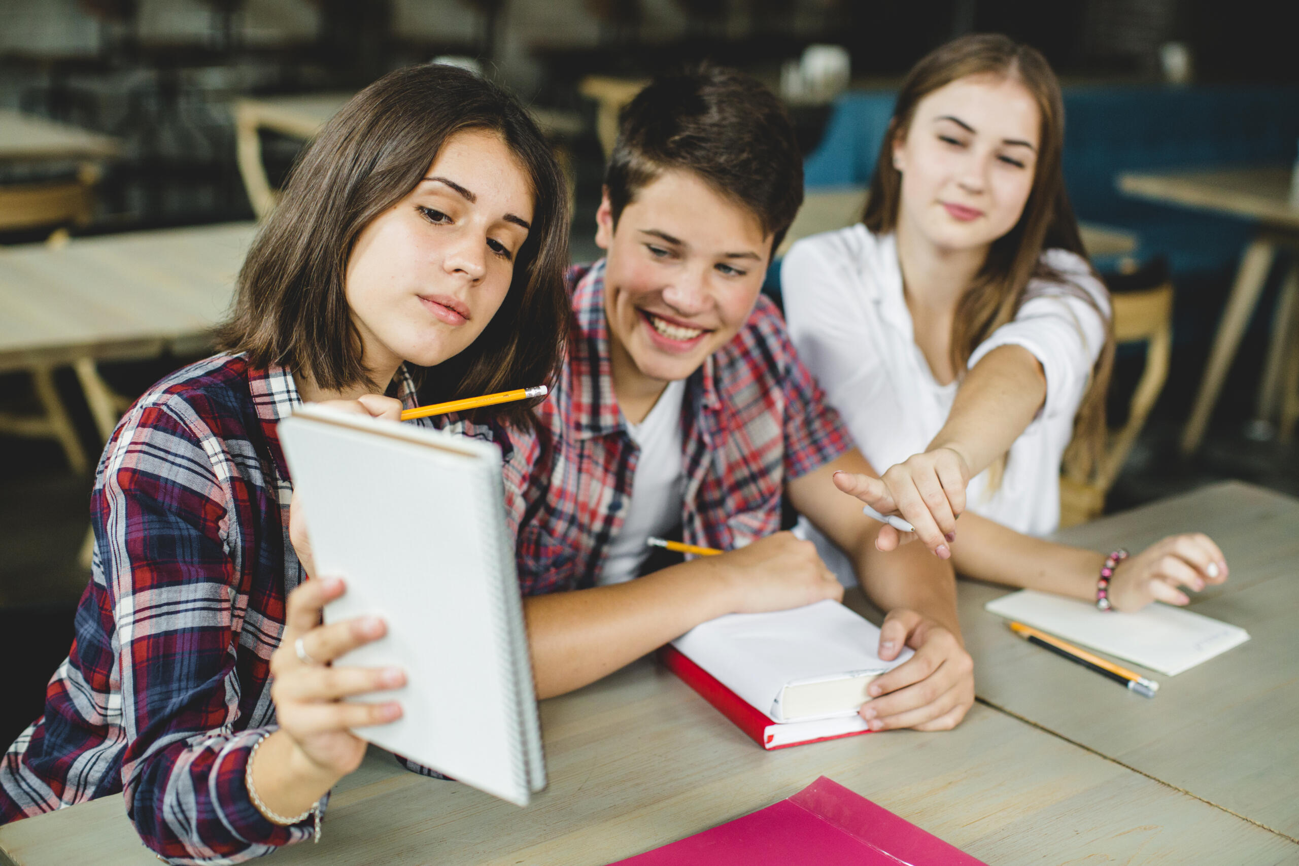 tres adolescentes estudiando juntos y señalando un cuaderno con los apuntes