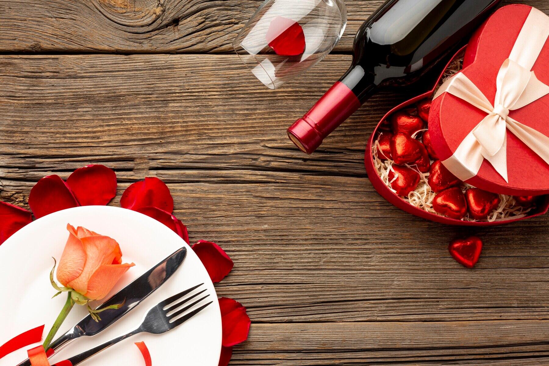 vista cenital de una mesa con plato y vino decorados con corazones y pétalos de rosas
