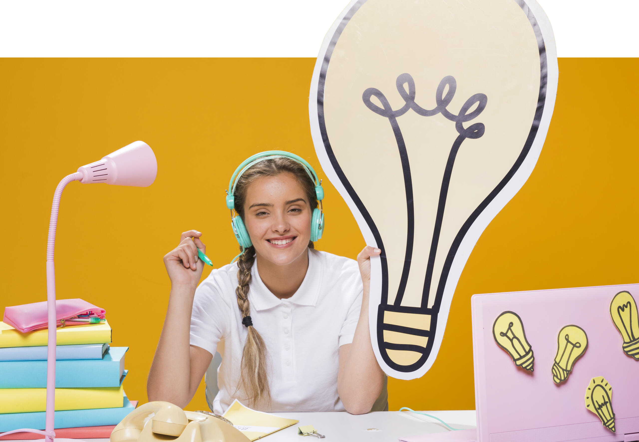 chica sonriente sosteniendo un gran foco de idea que sobresale la imagen, tiene libros y laptop sobre su escritorio