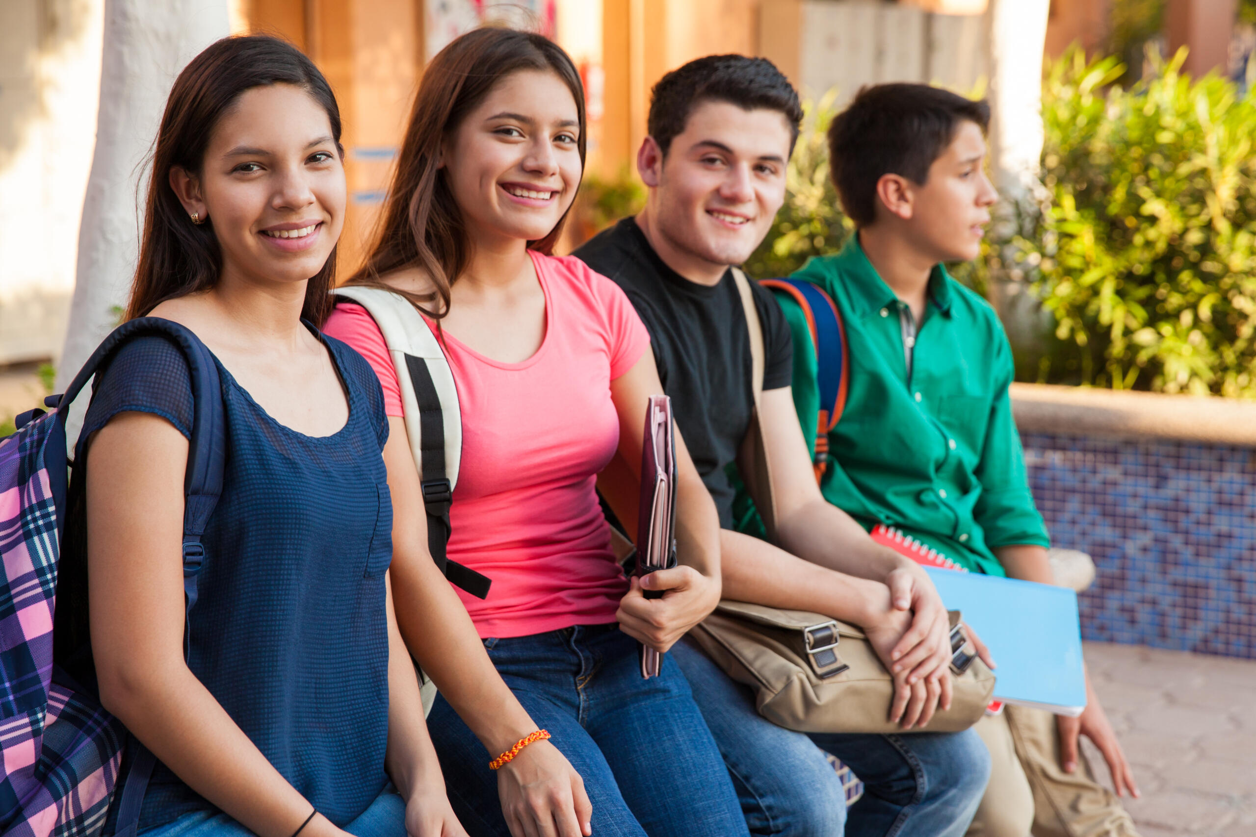 grupo de cuatro estudiantes con sus mochilas y cuadernos mirando sonrientes a la cámara