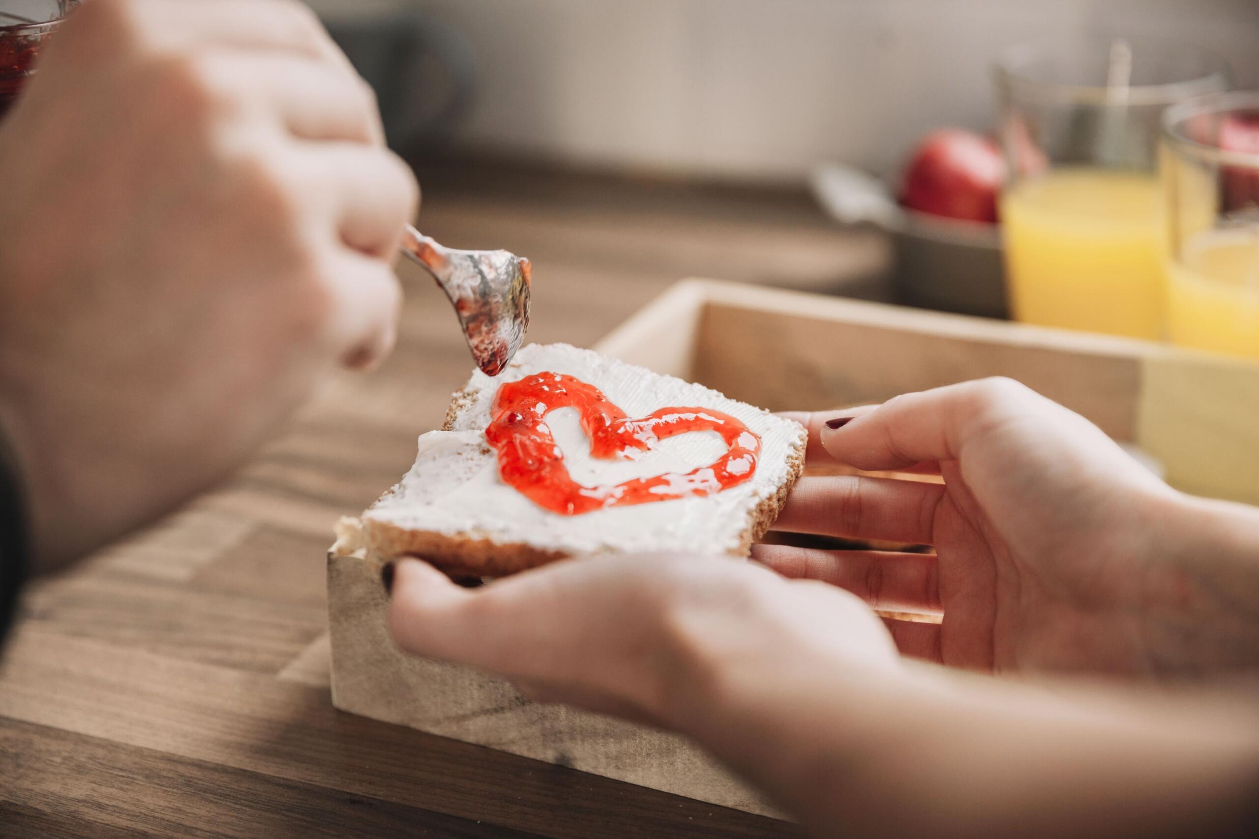 manos decorando una tostada con un corazon hecho de mermelada