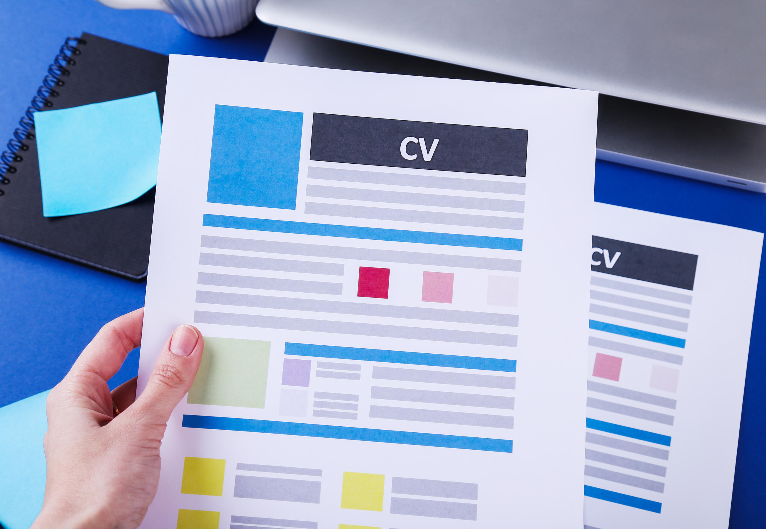 vista cenital de una mano sosteniendo una hoja CV con bloques coloridos