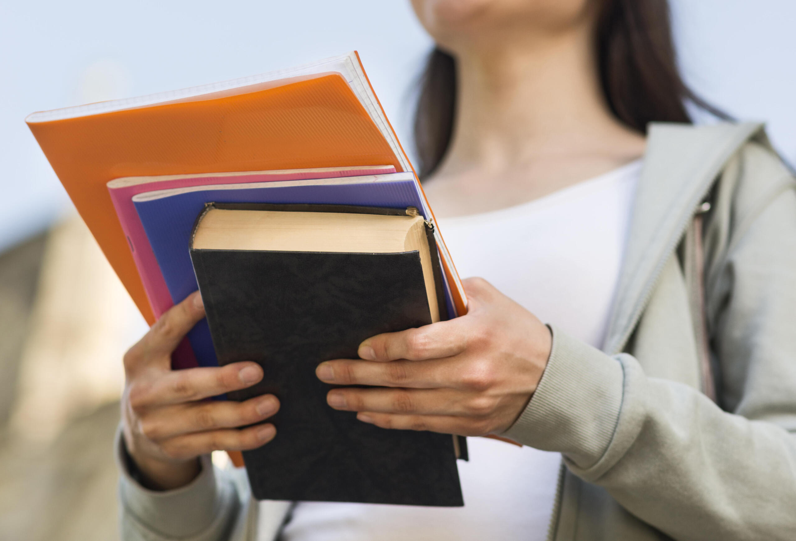 vista contrapicada de libros en primer plano sostenidos por una chica a la que no se le ve el rostro
