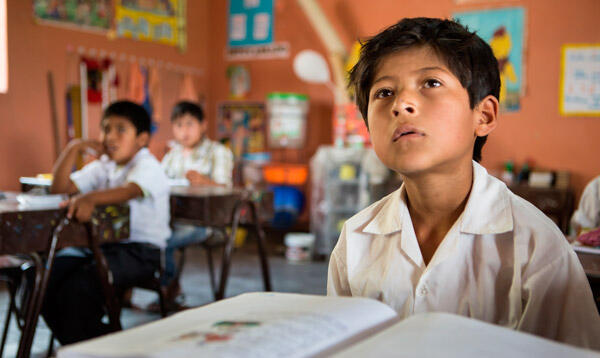 niño concentrado mirando a la clase con su libro en la carpeta y otros alumnos de fondo