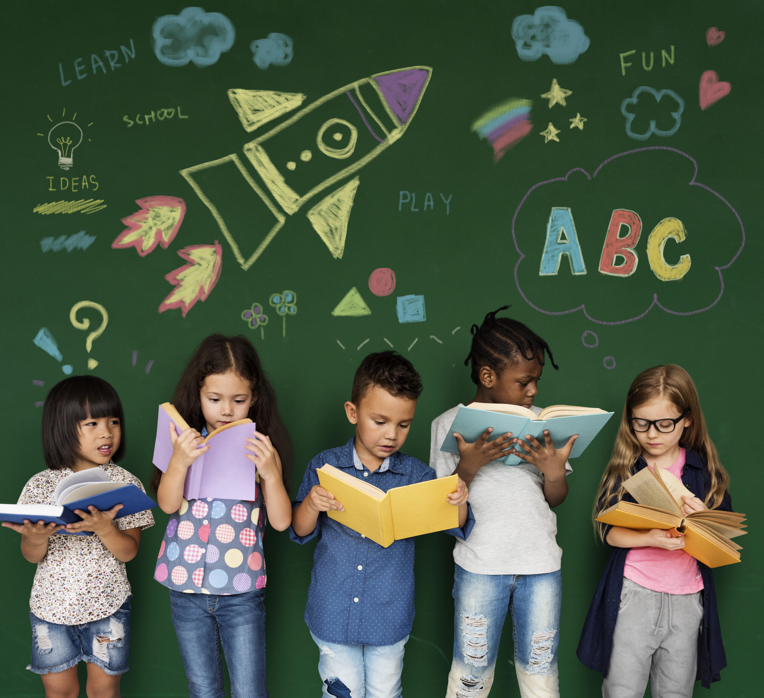 cinco niños leyendo libros con un fondo de pizarra verde y dibujitos hechos en tiza de fondo