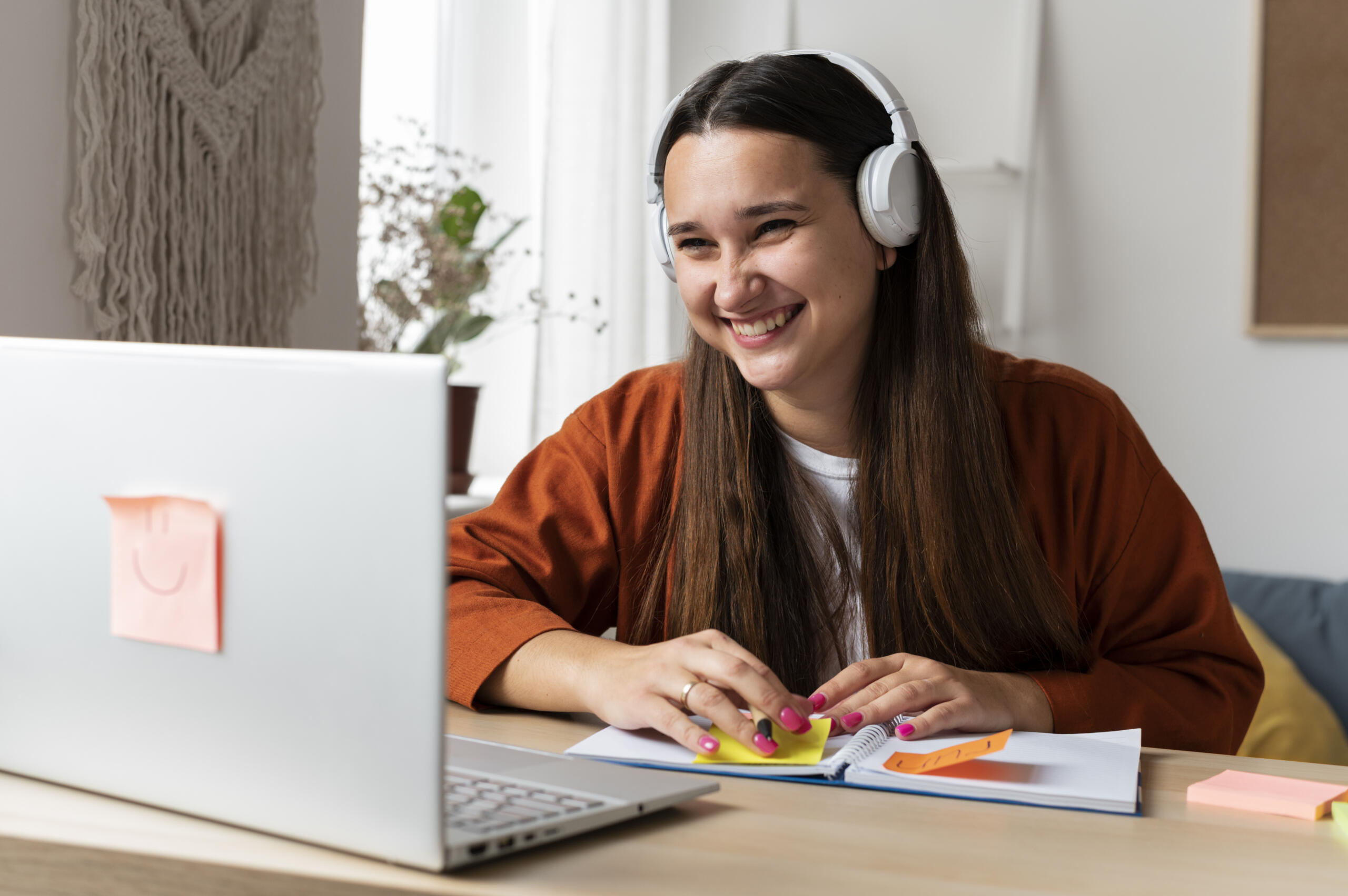 chica sonriente en una videollamada con su laptop y post-its en su escritorio.