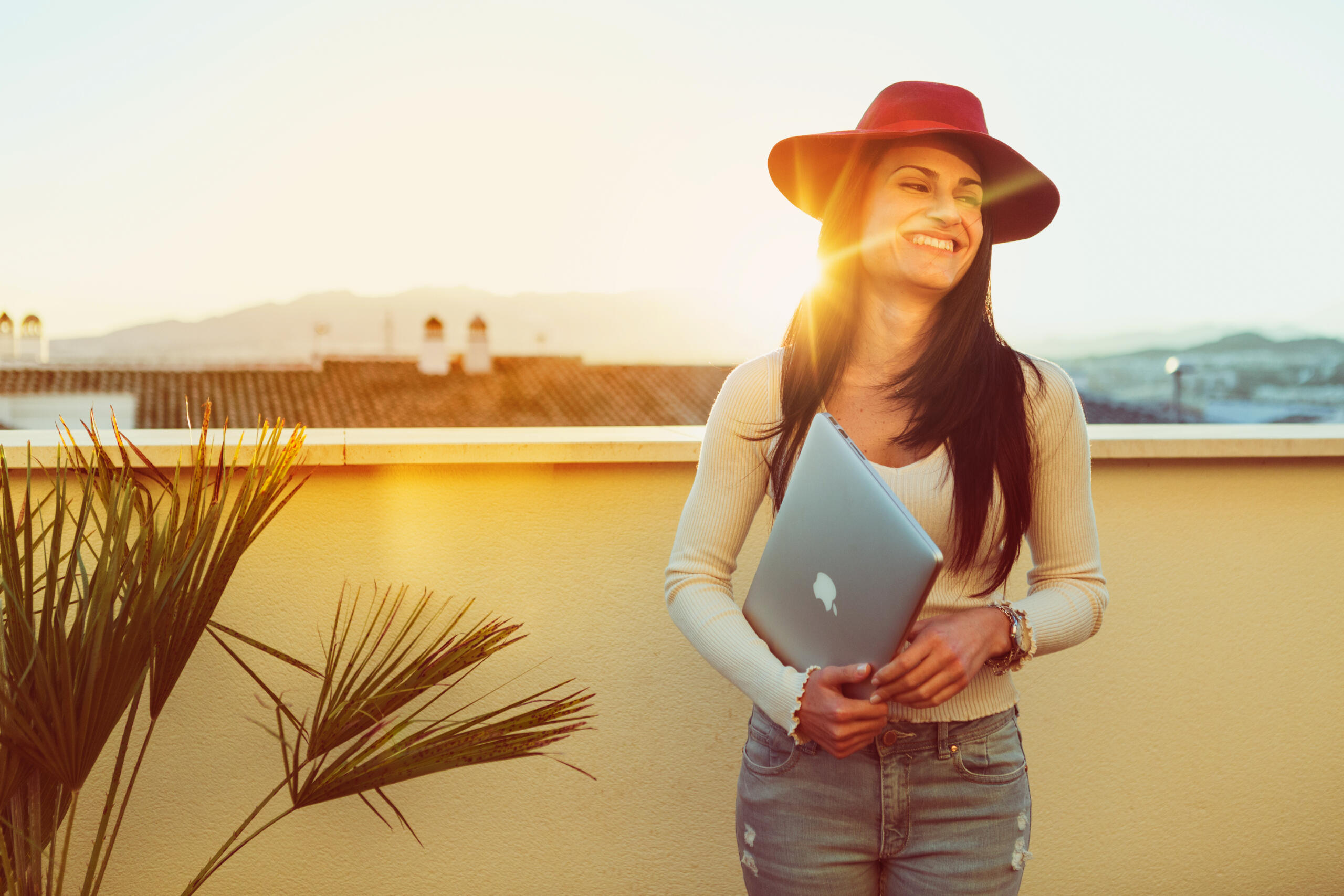 chica sonriente con su laptop en una terraza con el sunset iluminando tras ella
