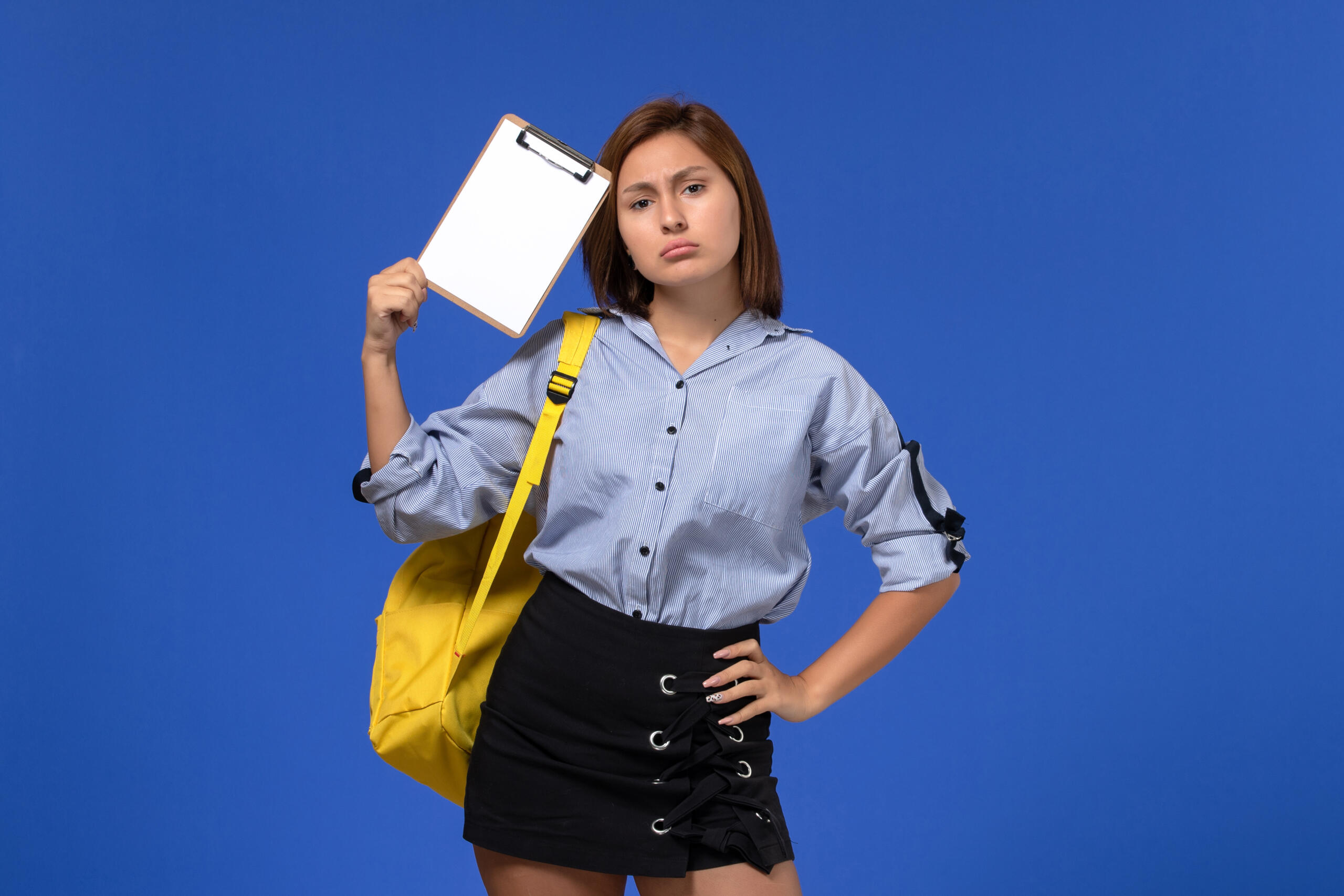 chica con rostro preocupado en fondo azul, sosteniendo un tablero formulario pegado a la cabeza