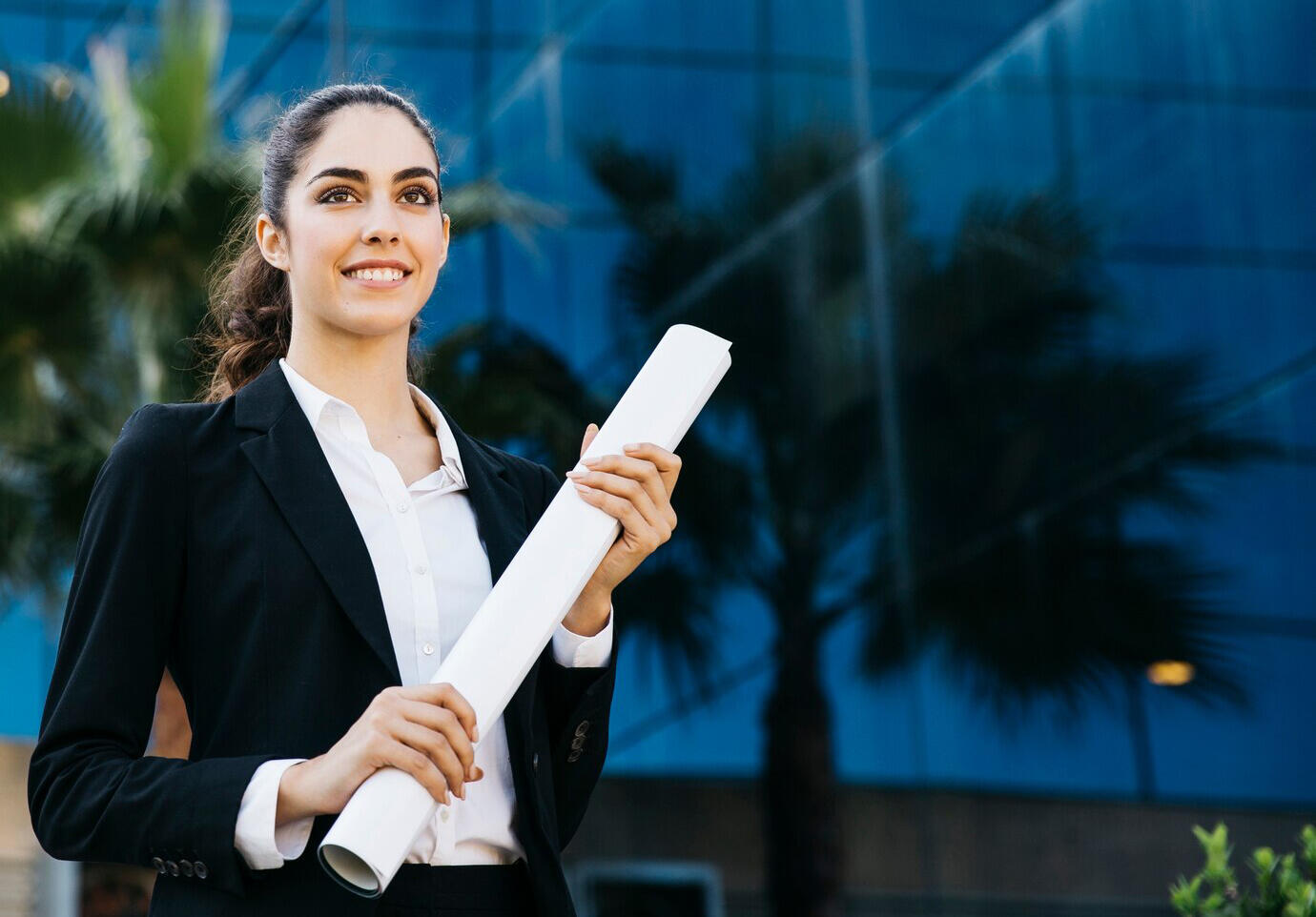 chica sonriente con traje elegante mirando al frente con un documento enrrollado entre sus manos