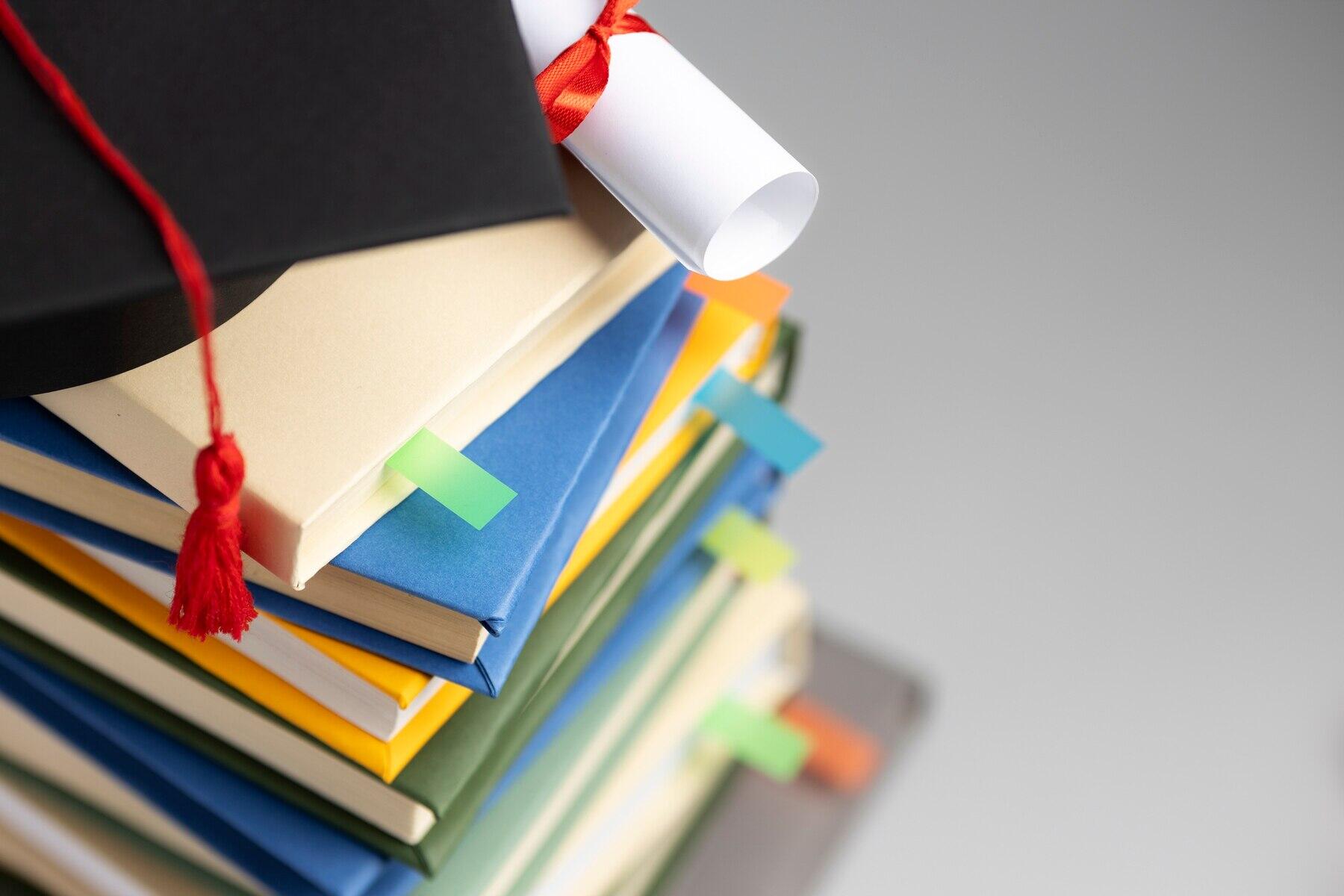 vista cenital de birrete y diploma sobre una torre de libros y folios