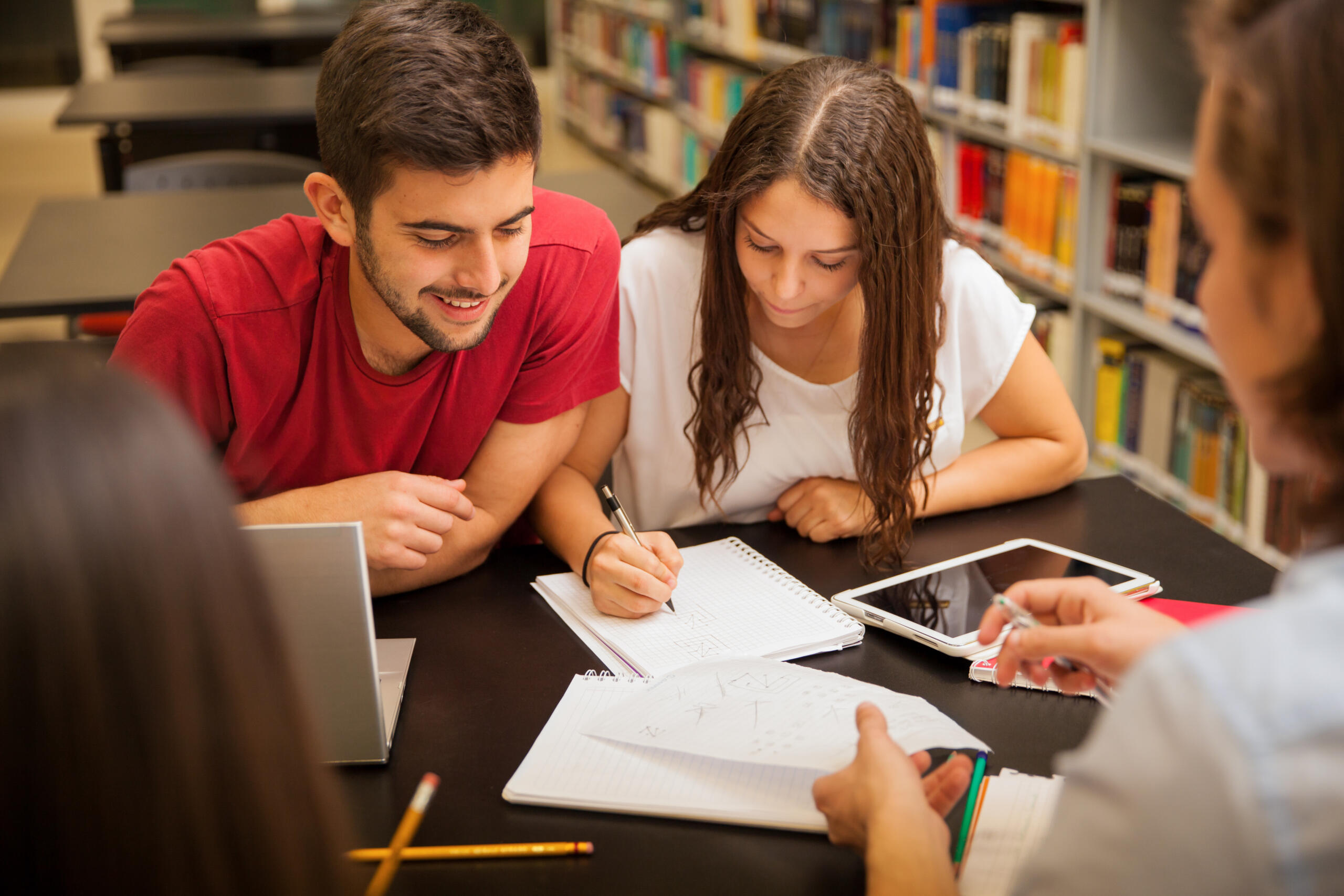 grupo de estudiantes reunidos en una misma mesa en medio de una biblioteca