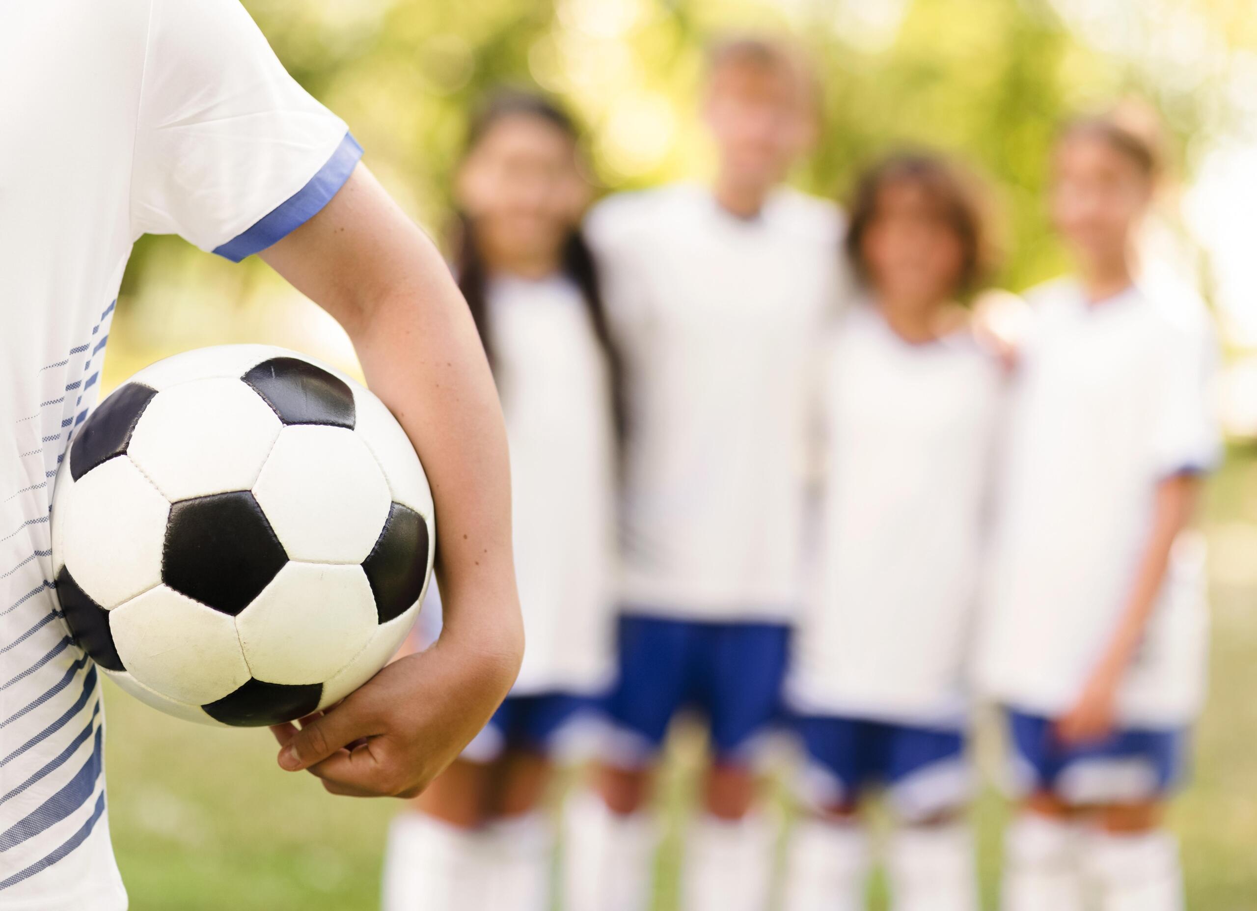 vista primer plano de torso de niño sujetando el balón bajo el brazo y cuatro niños de fondo desenfocado
