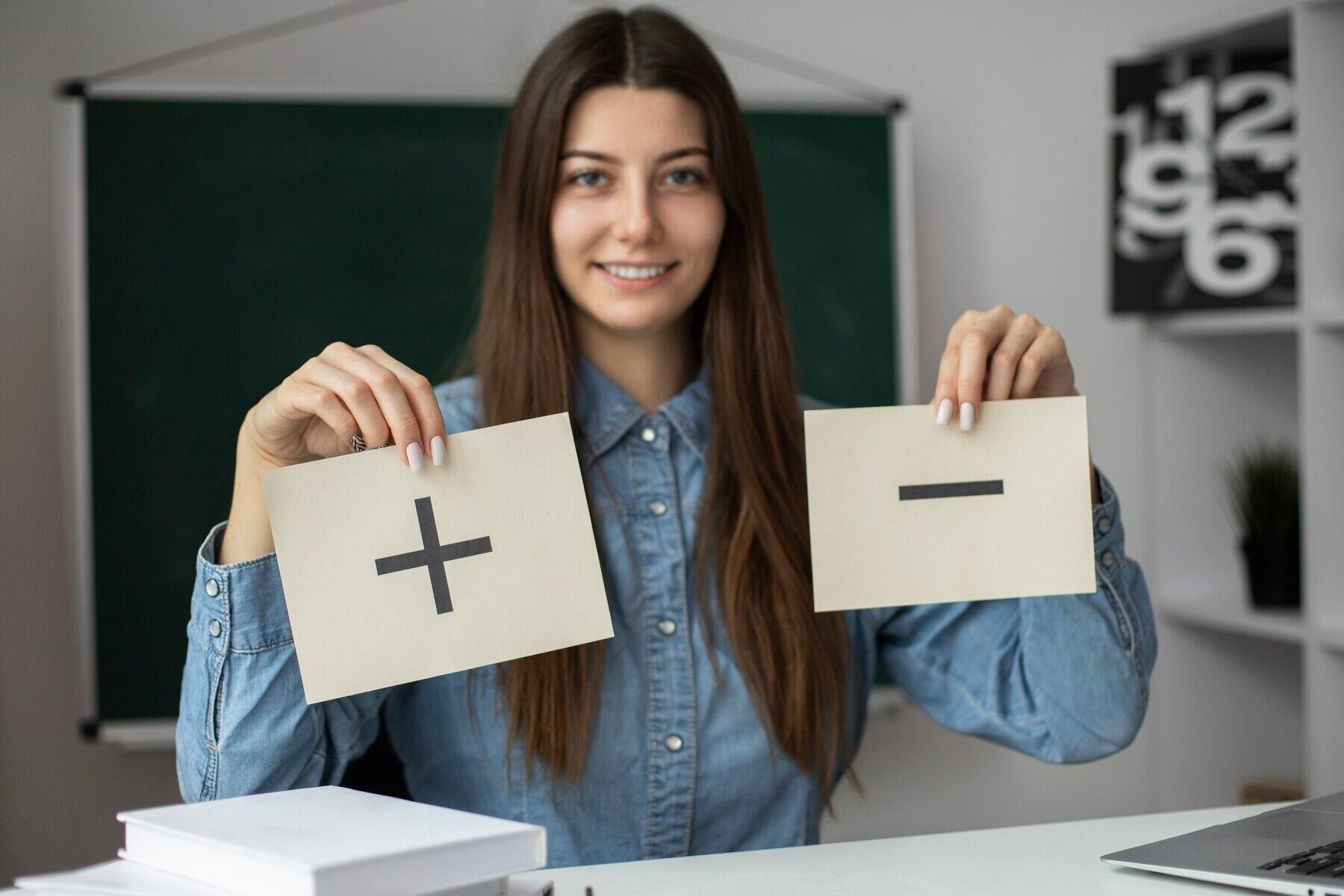 chica sonriente sosteniendo dos carteles en la mano con un + y un -