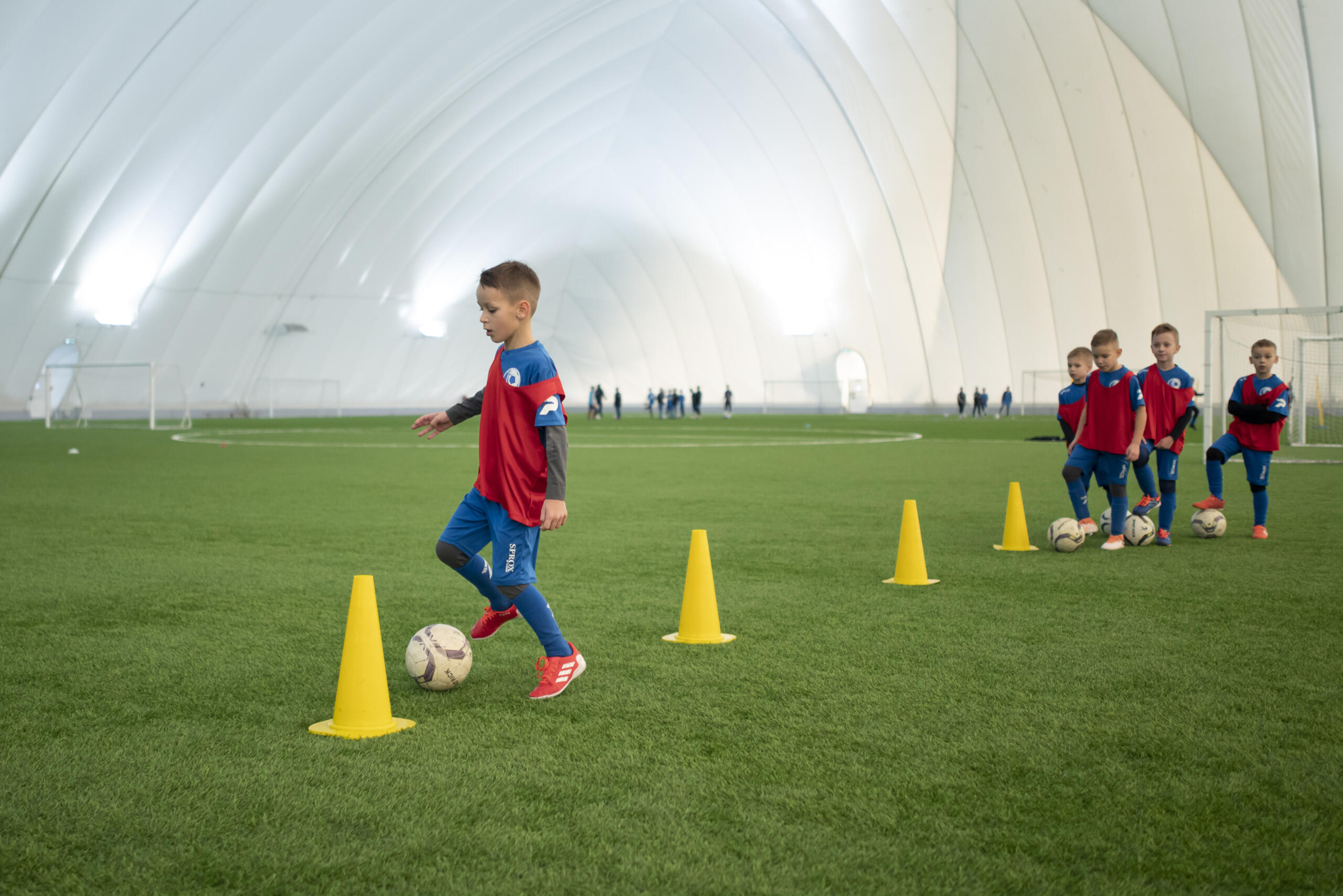 niños haciendo práctica de los conos con la pelota de fútbol