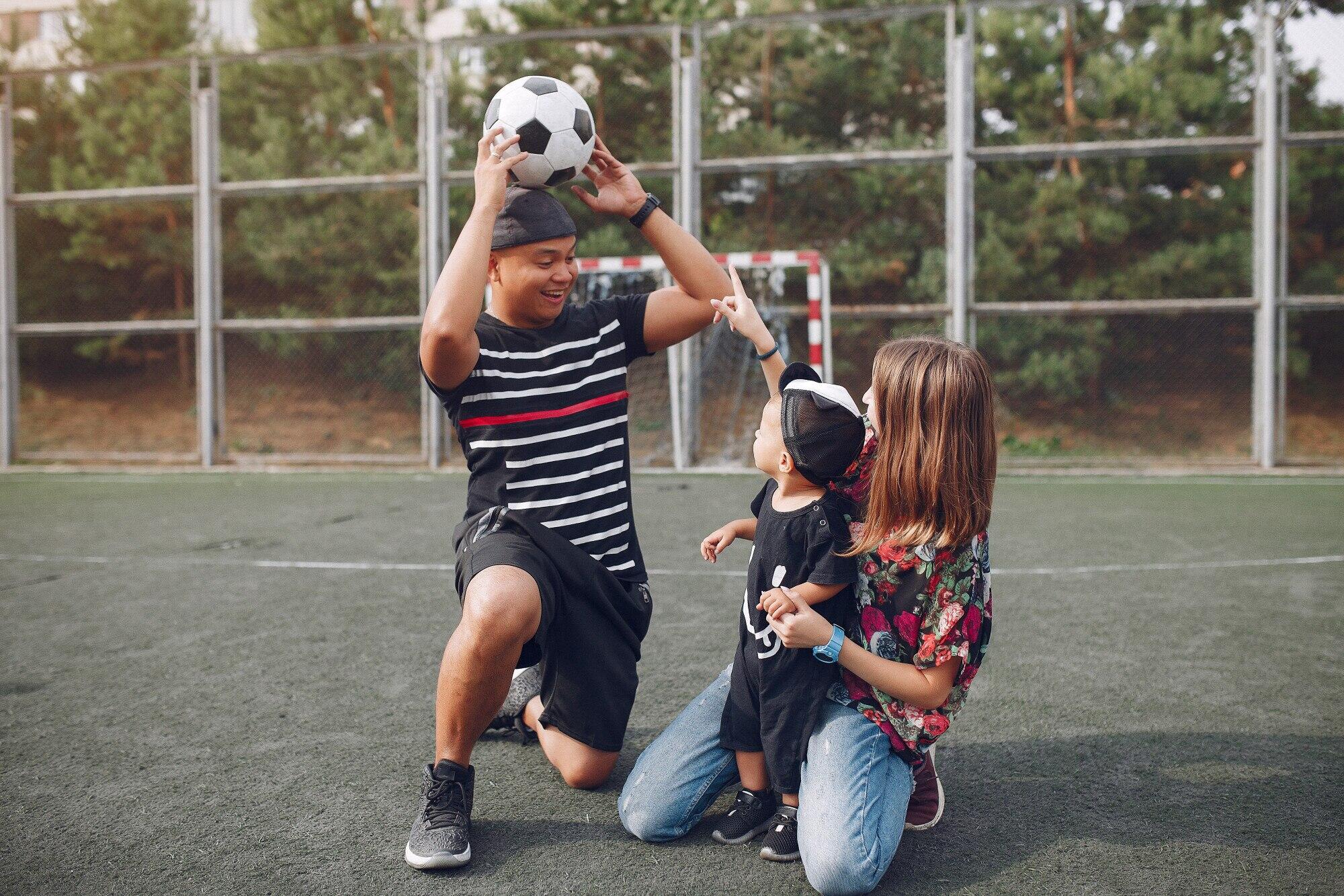 padres sonrientes mostrándole la pelota de futbol a su hijo pequeño en medio de una cancha