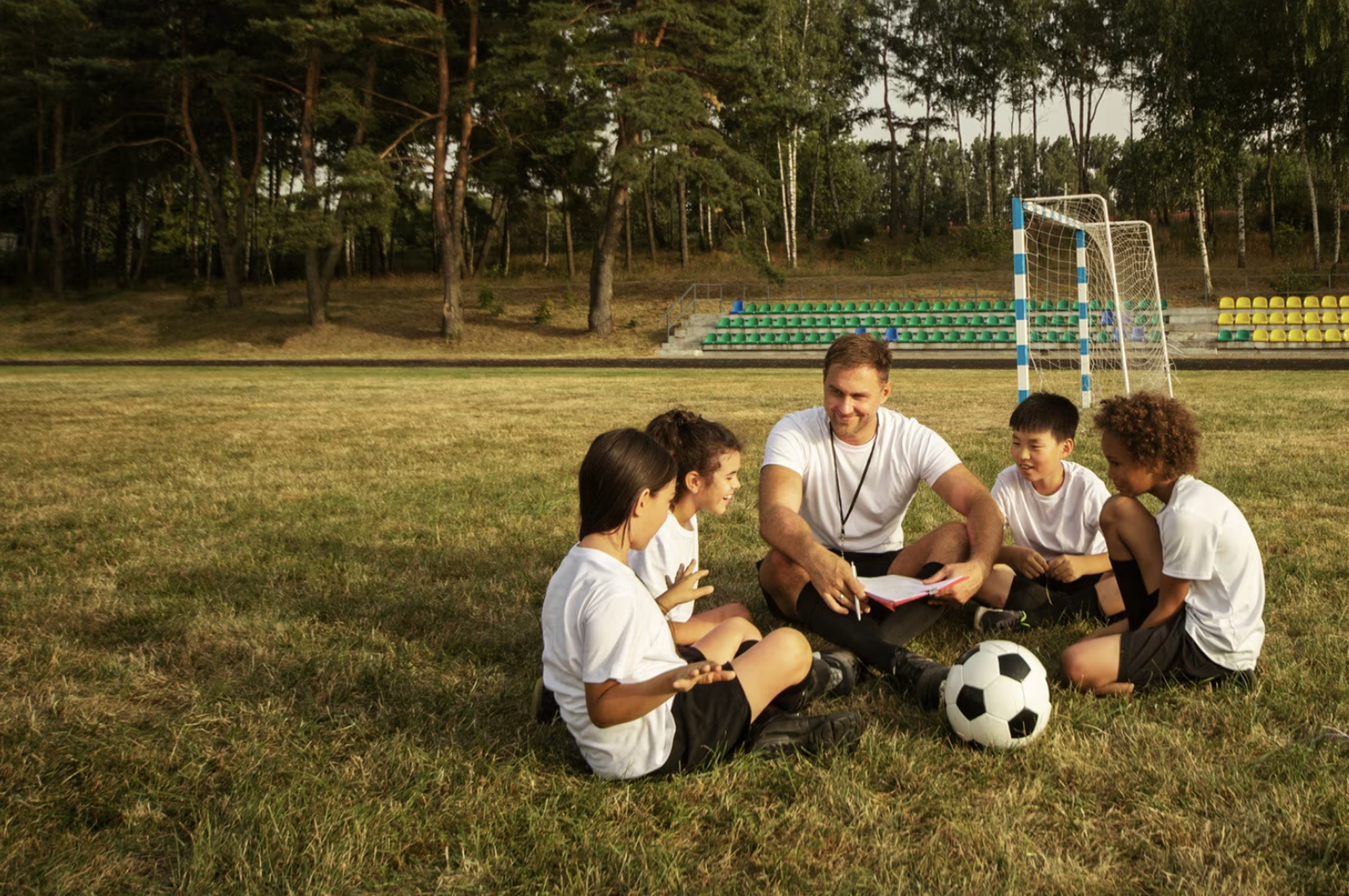 niños sentados en el campo de juego con su entrenador