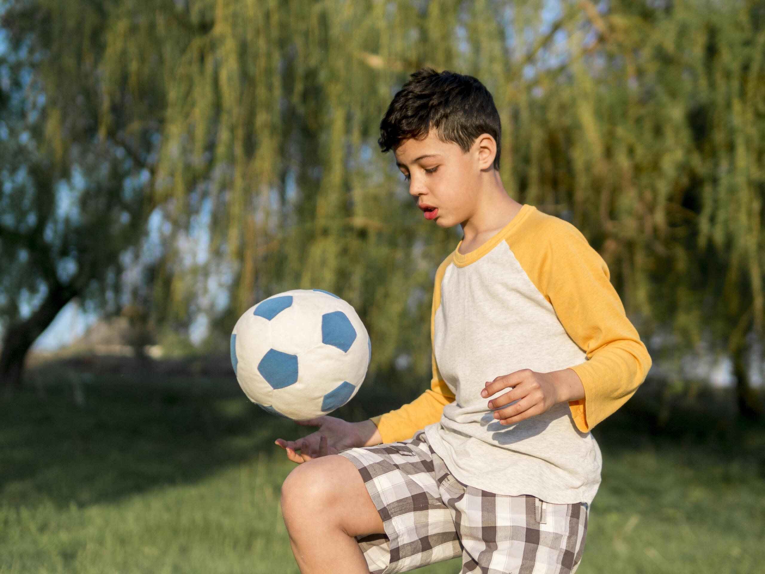 niño haciendo dominadas en la rodilla con una pelota de fútbol de juguete