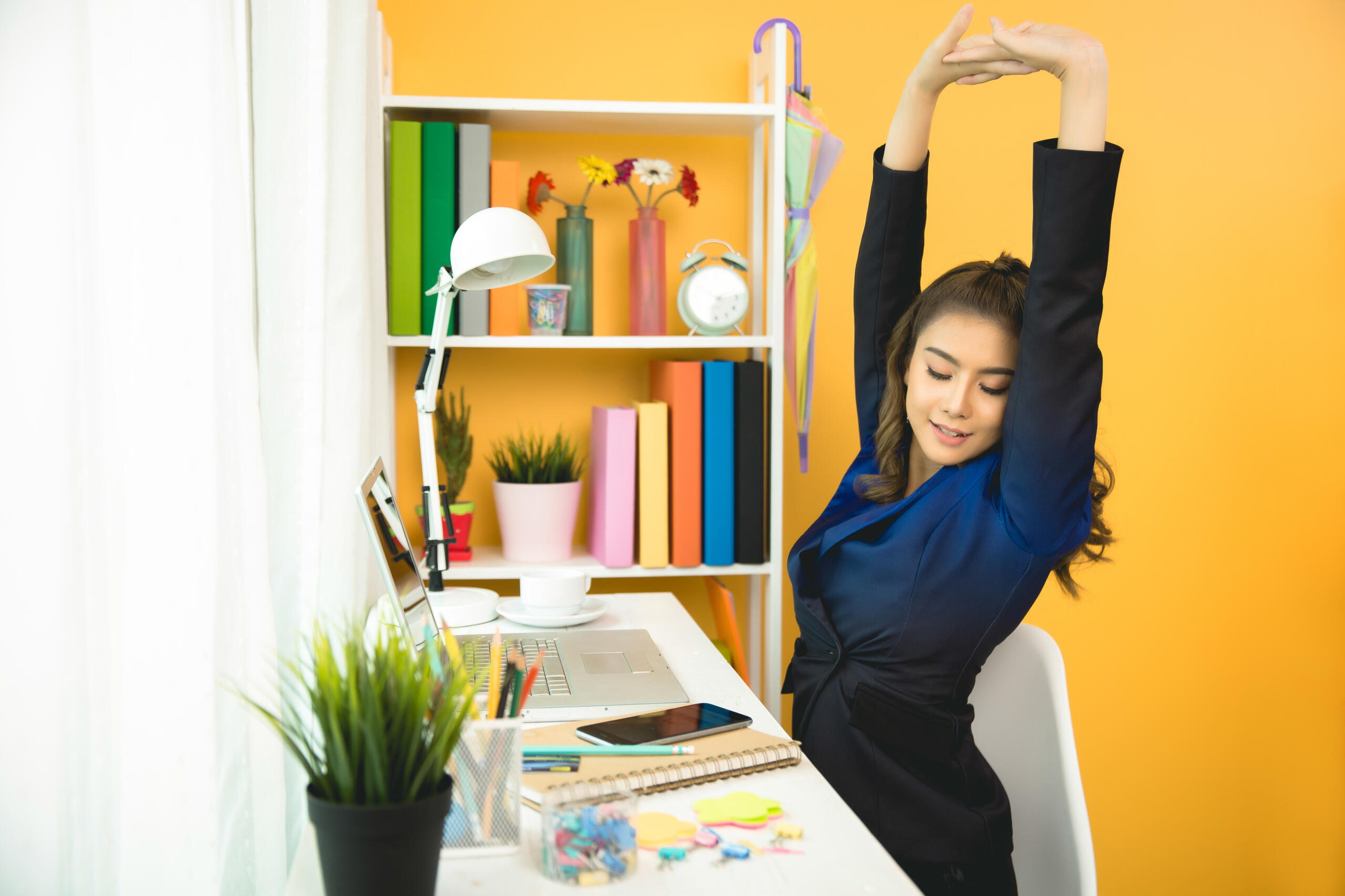 chica estirando ambos brazos hacia arriba sentada frente a su escritorio