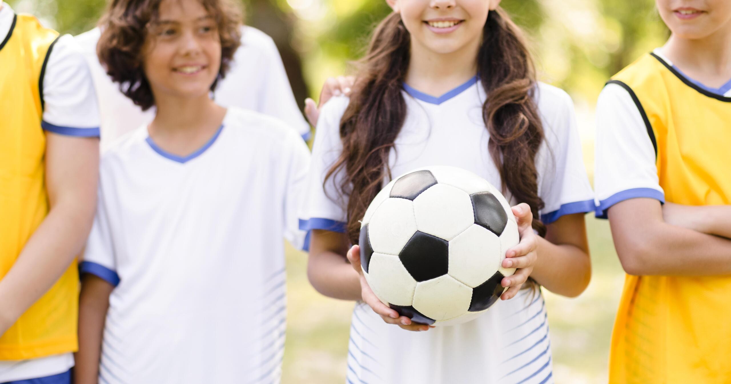 niños en fila sonrientes y una niña en medio sosteniendo la pelota de fútbol