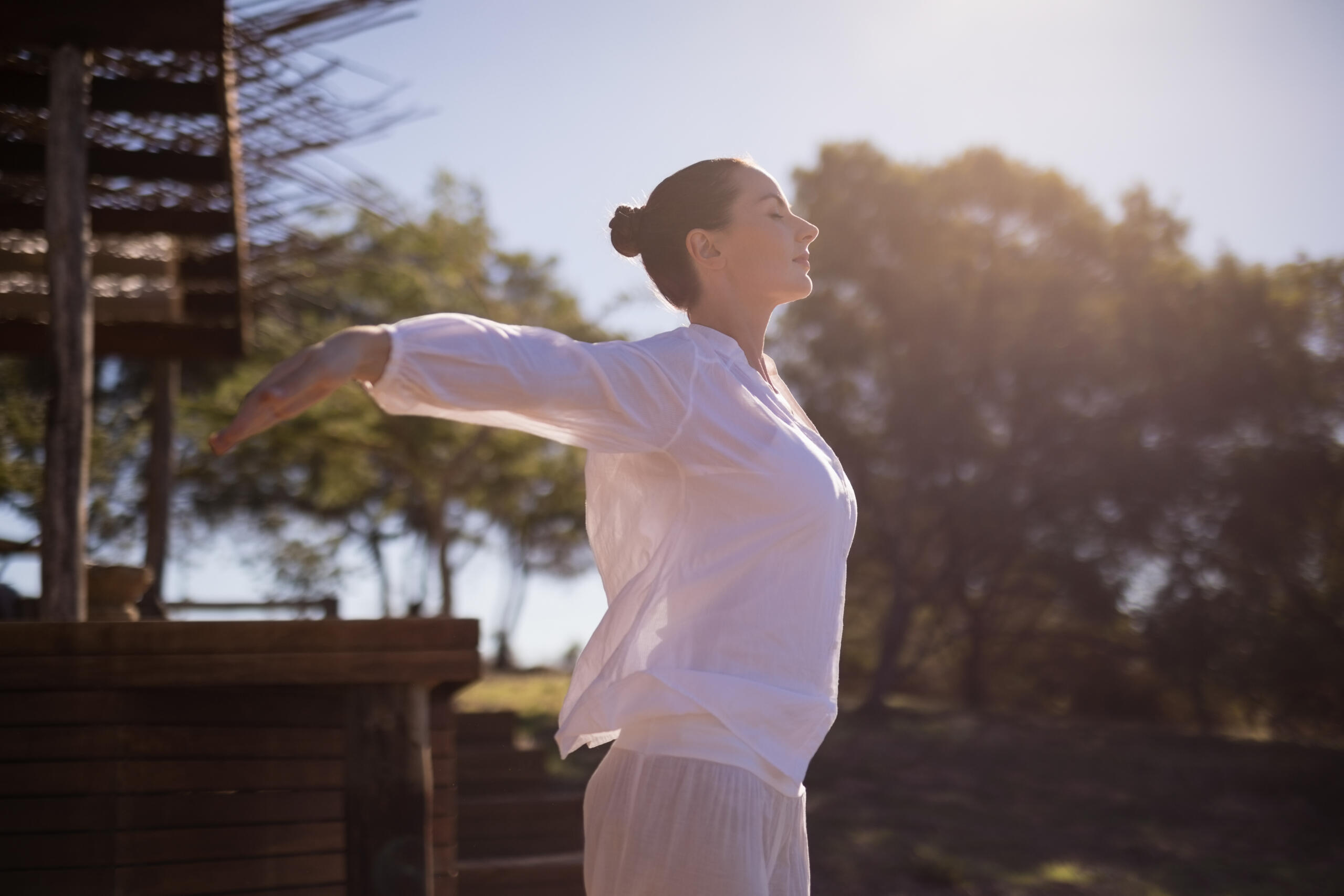 mujer vestida de blanco con los brazos extendidos hacia los lados y los ojos cerrados en un jardín