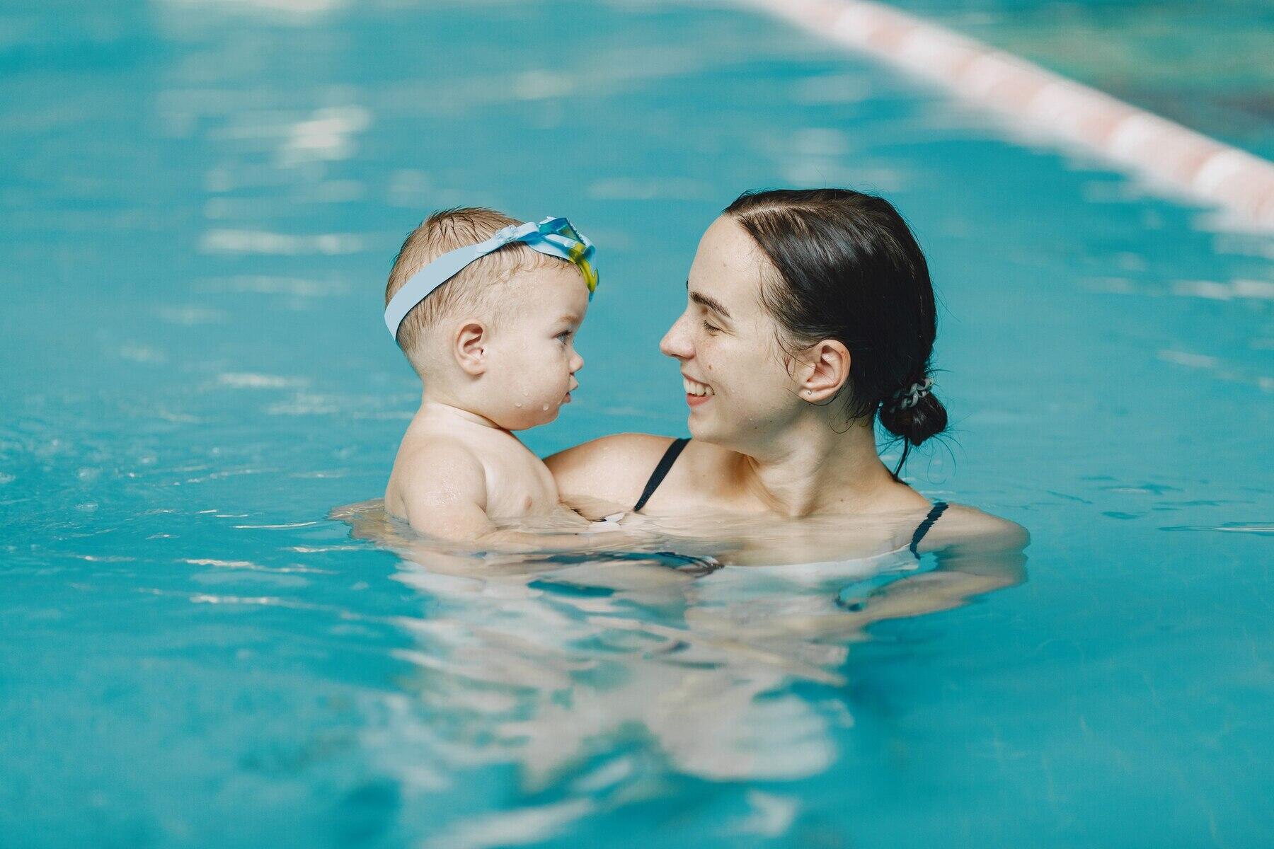 mama sonriente cargando a su bebé en la piscina