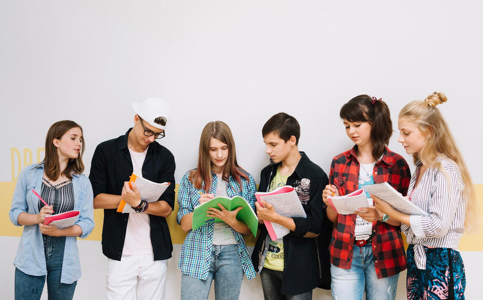 grupo de seis adolescentes con sus cuadernos haciendo anotaciones de pie