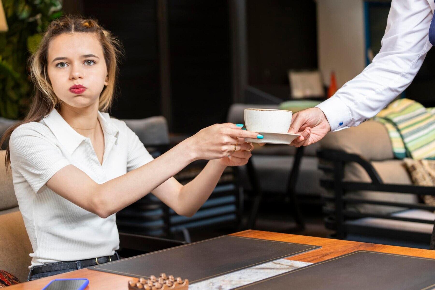 chica devolviendo una taza del café al mesero con cara de desagrado