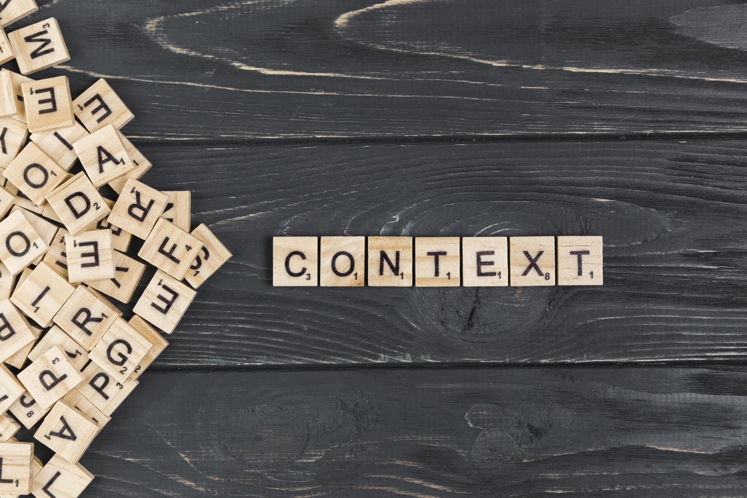 scrabble sobre una mesa con la palabra CONTEXT armada y el resto de fichas apiladas al lado izquierdo.