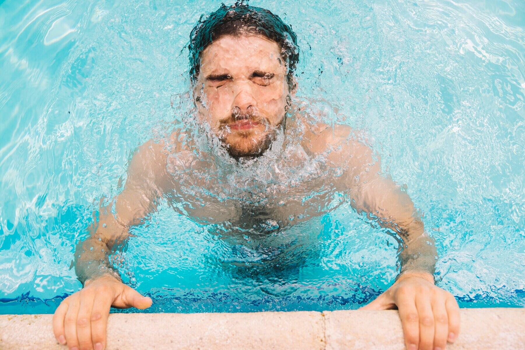vista cenital de chico sujeto al borde de la piscina buceando con la cabeza poco sumergida