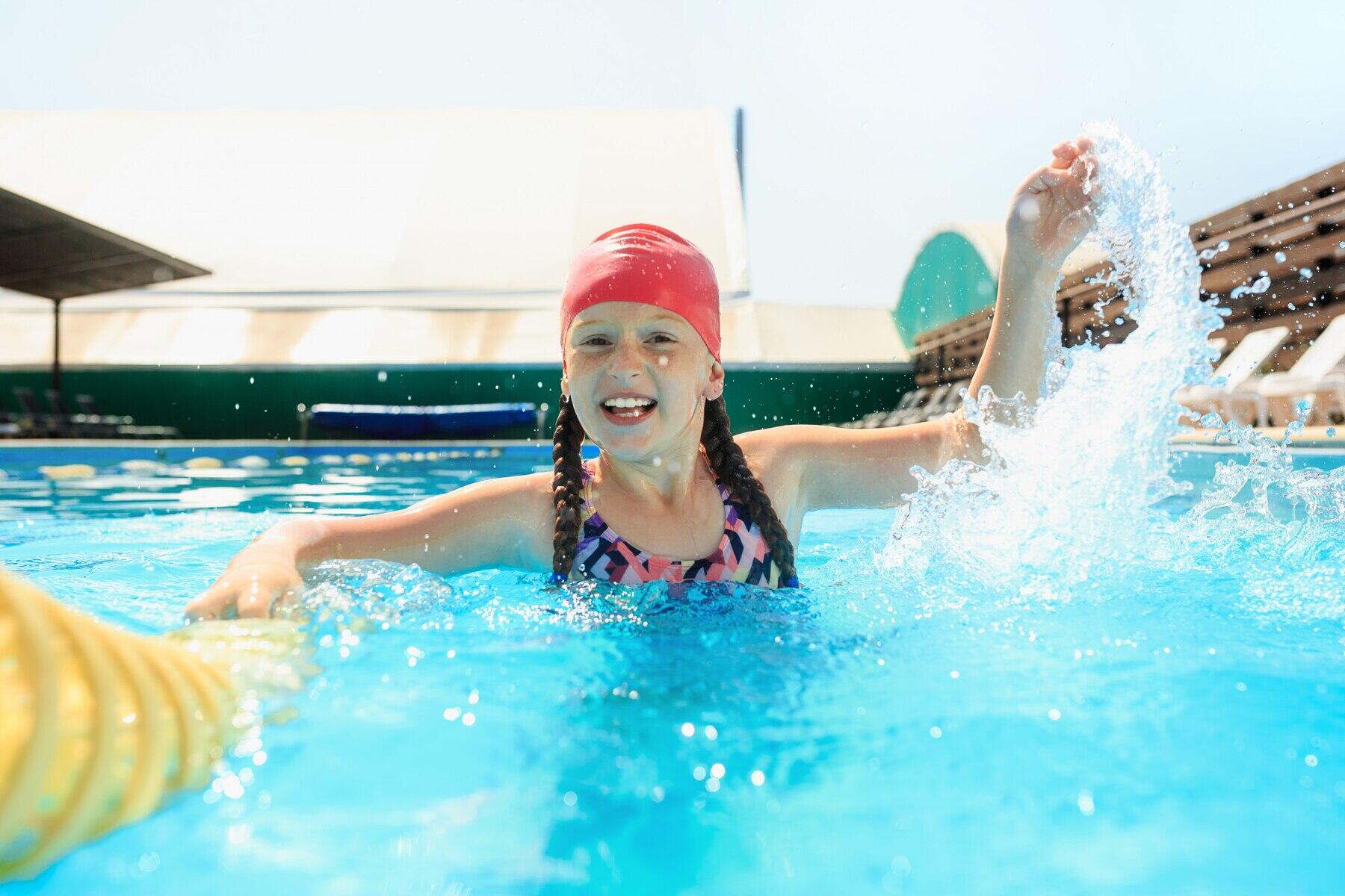 niña con gorrita de natación sonriente mirando a la cámara mientras juega con el agua con una mano