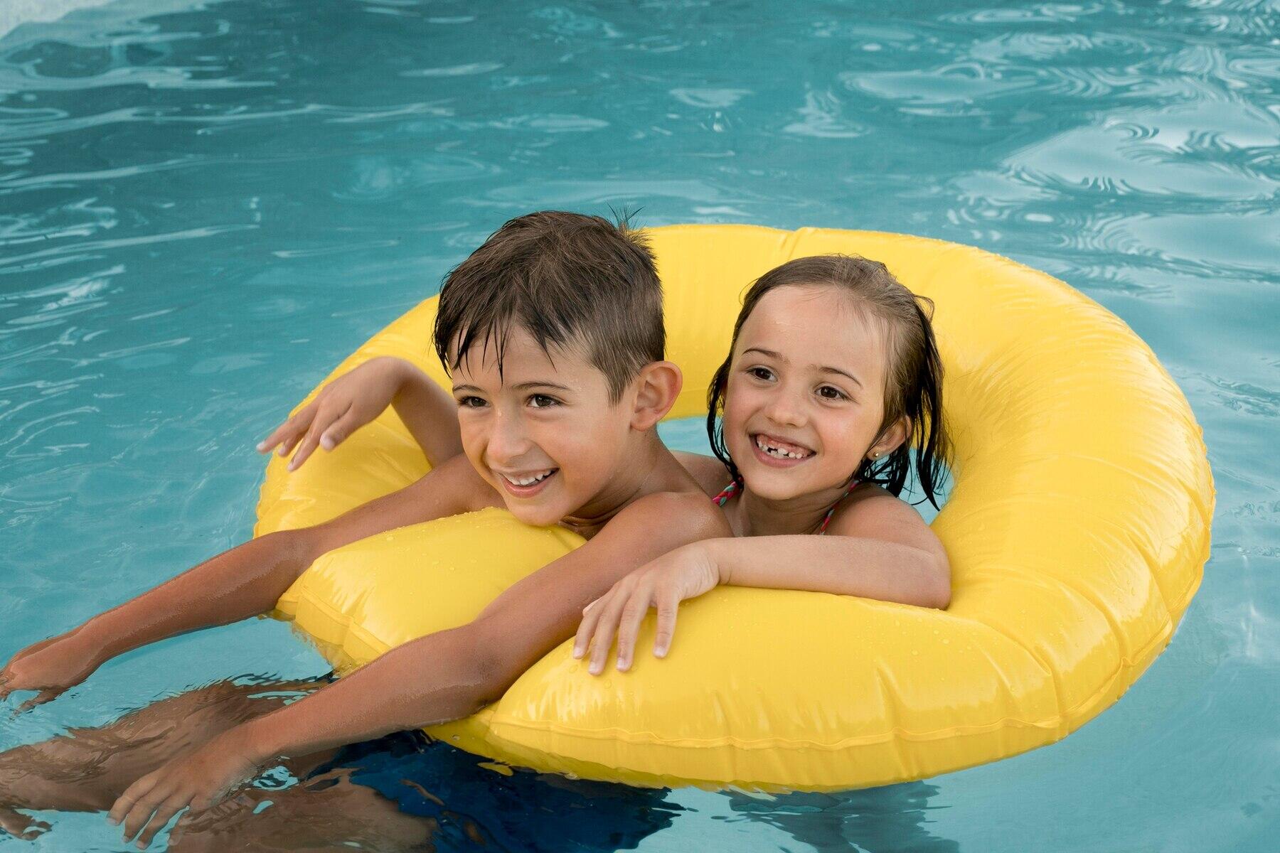 dos niños sonrientes dentro de un flotador amarillo donut en la piscina