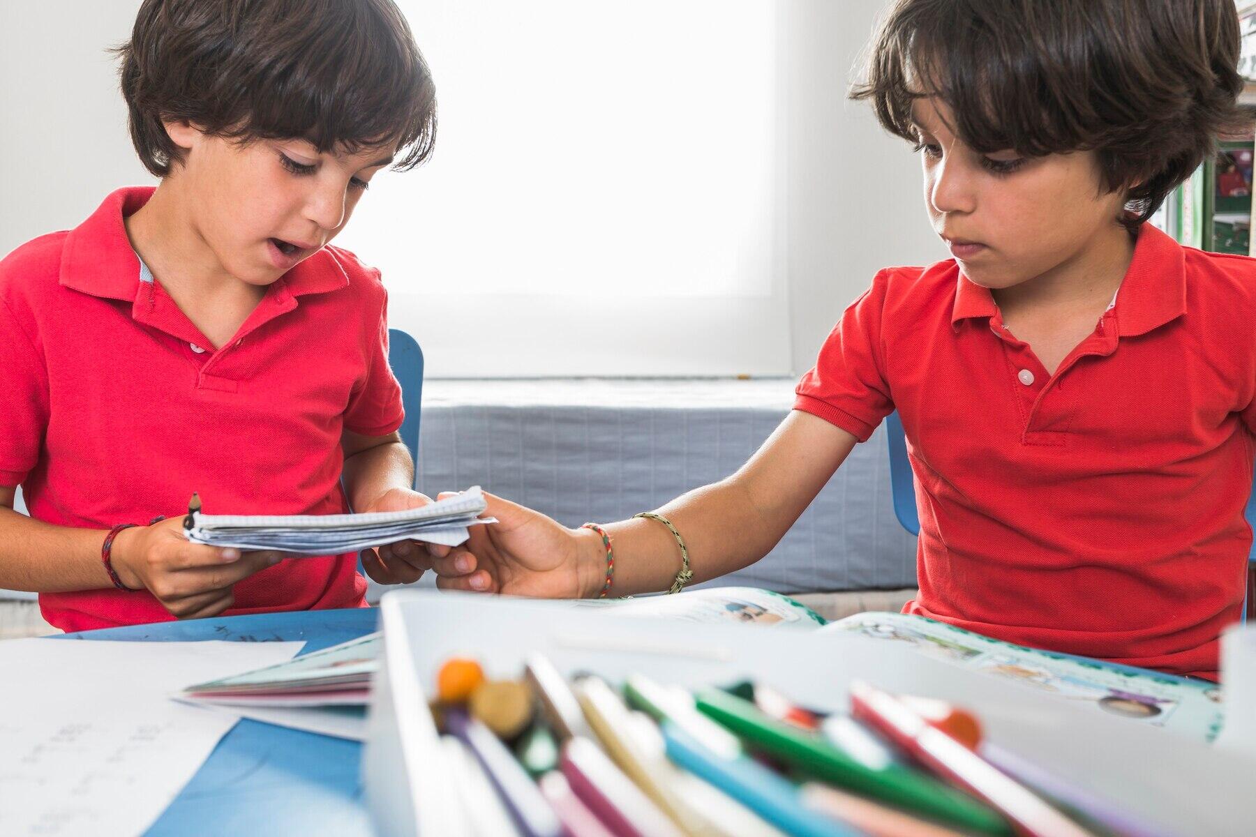 dos niños prestándose hojas con sus colores y libros sobre la mesa