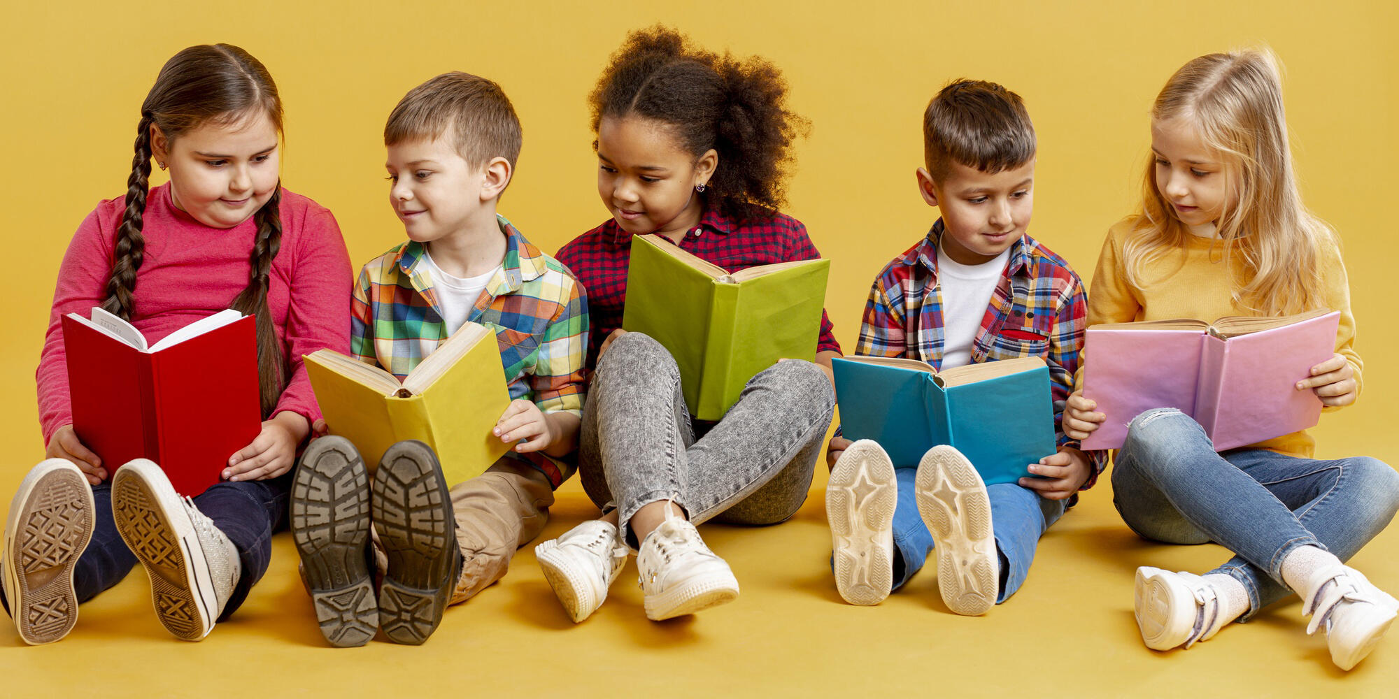 cinco niños leyendo libros de colores sentados sobre un fondo amarillo