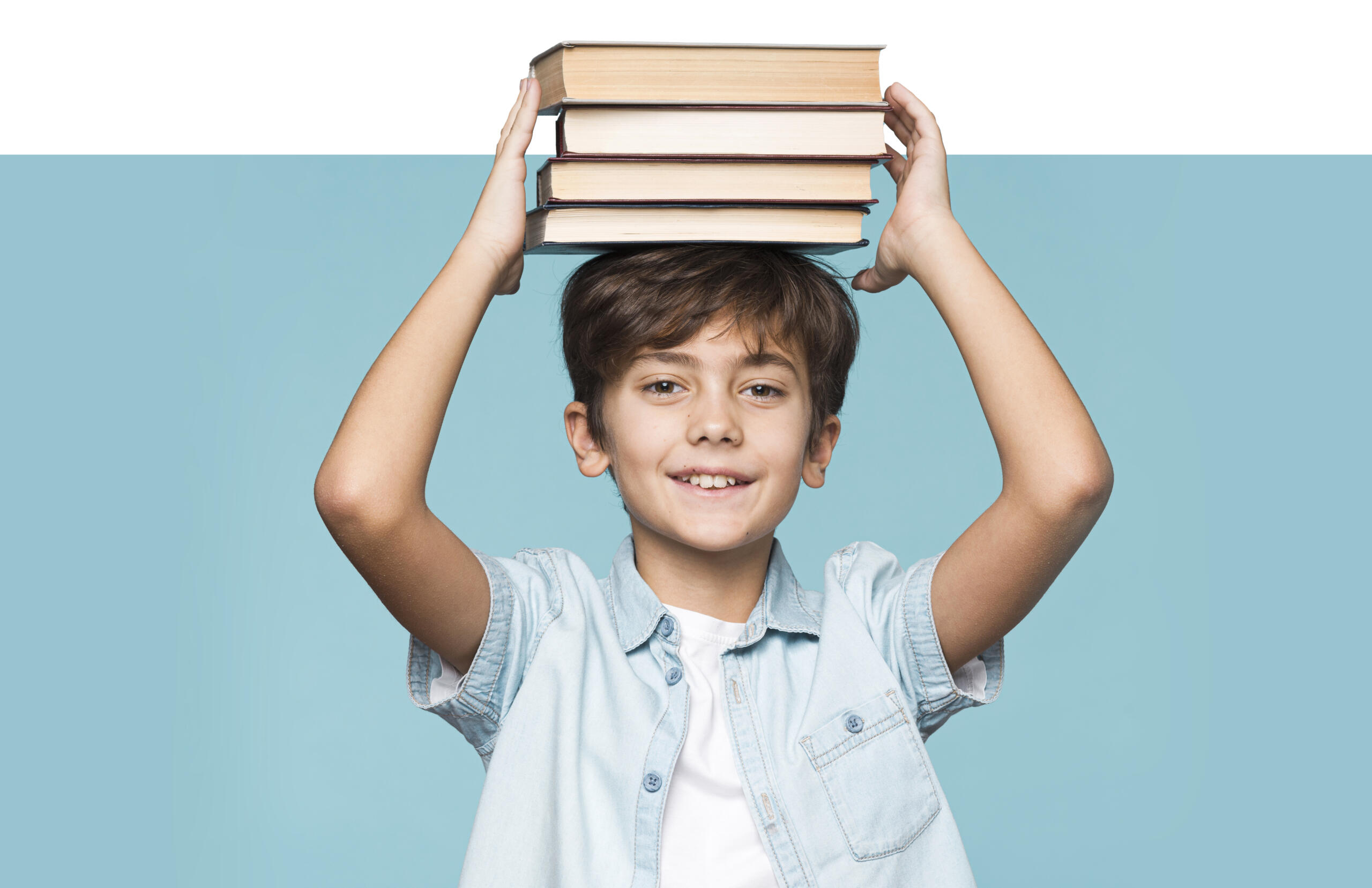 niño sonriente sosteniendo con ambas manos unos cuatro libros sobre la cabeza