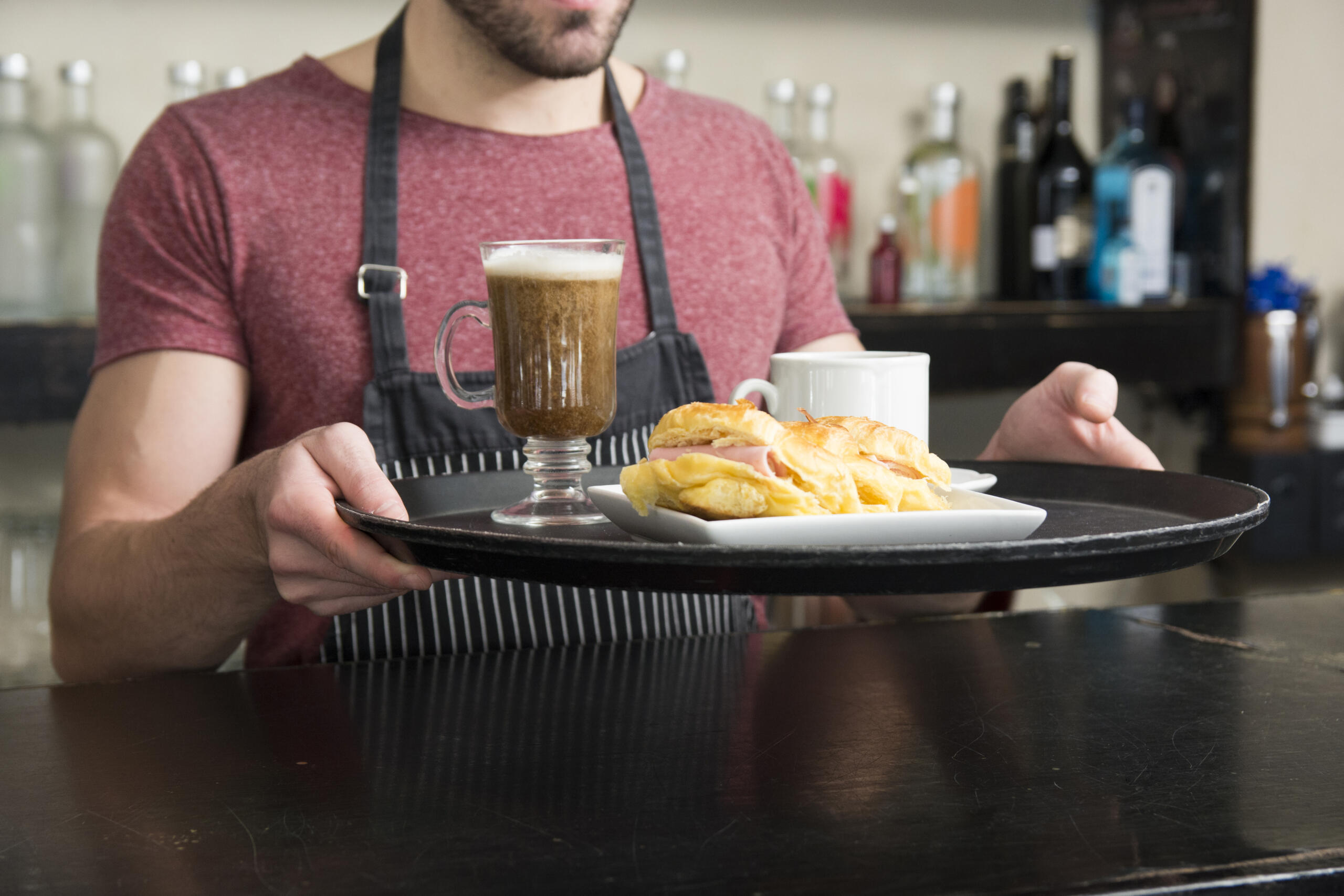 vista de un mesero sujetando una bandeja con un pedido de café y sandwich