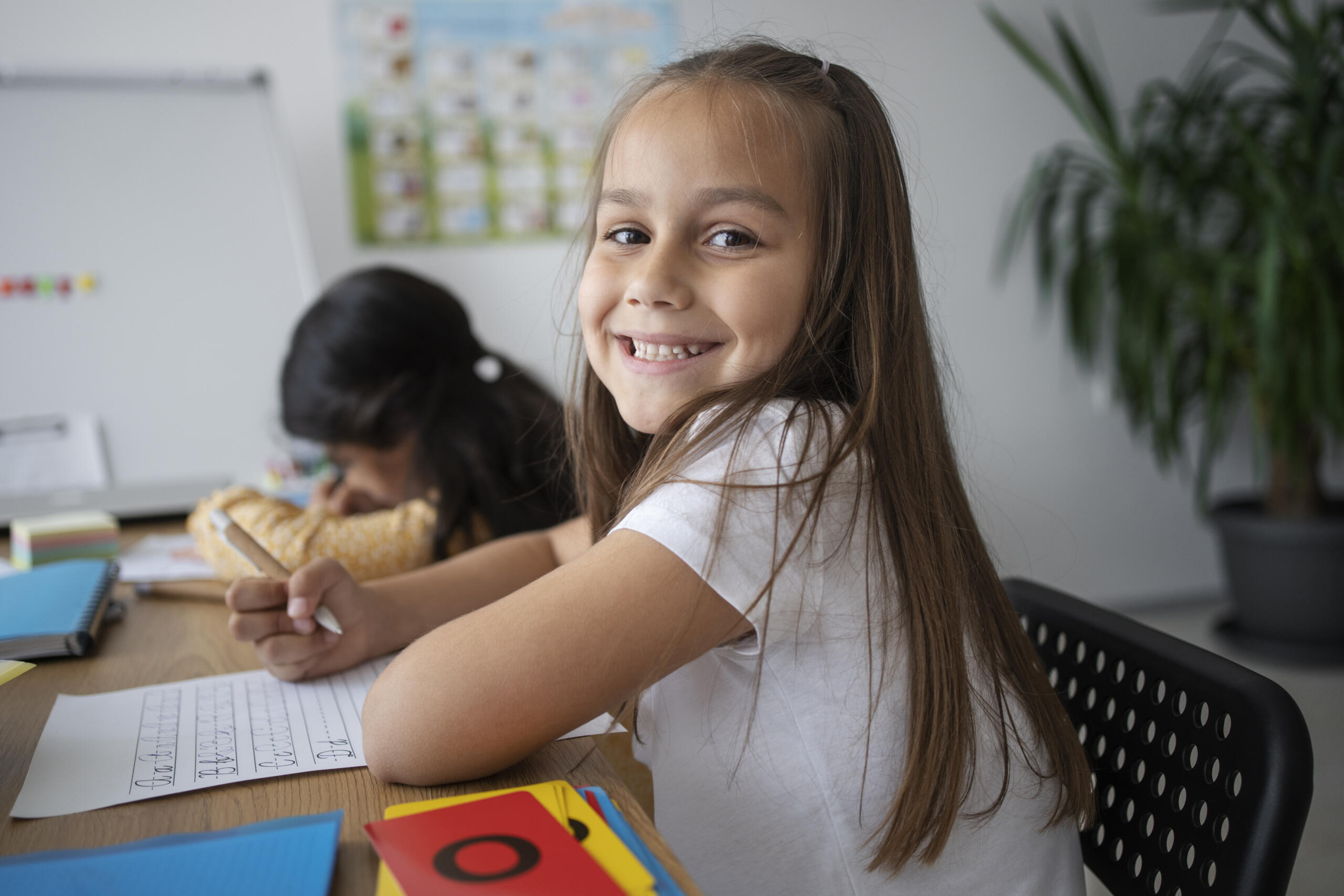 niña en su carpeta de escuela mirando sonriente a la camara mientras escribe