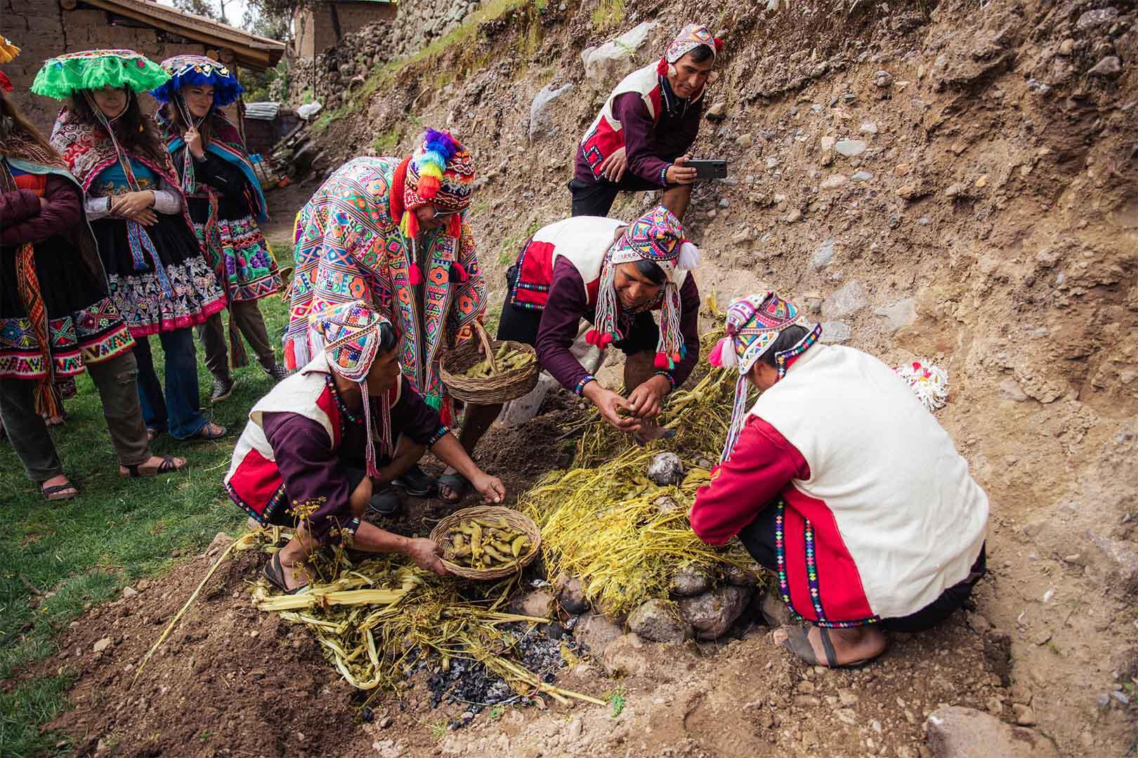 grupo de personas con trajes tipicos preparando una pachamanca en la tierra