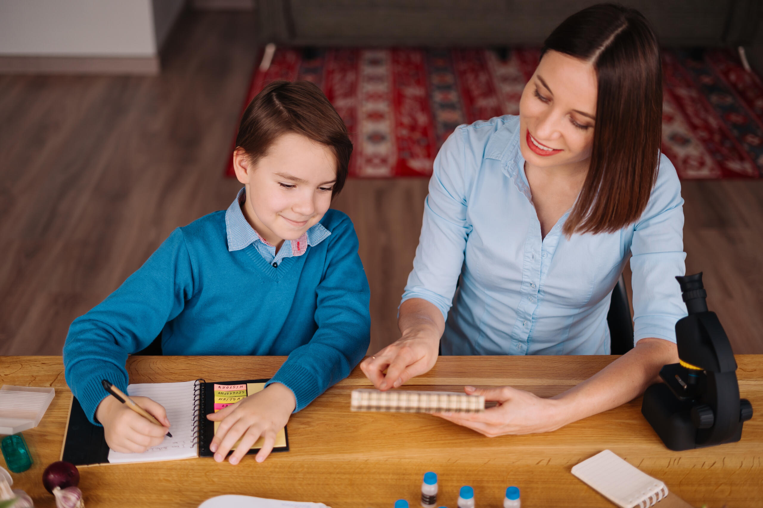 niño junto a su profesora revisando una libreta y tomando notas