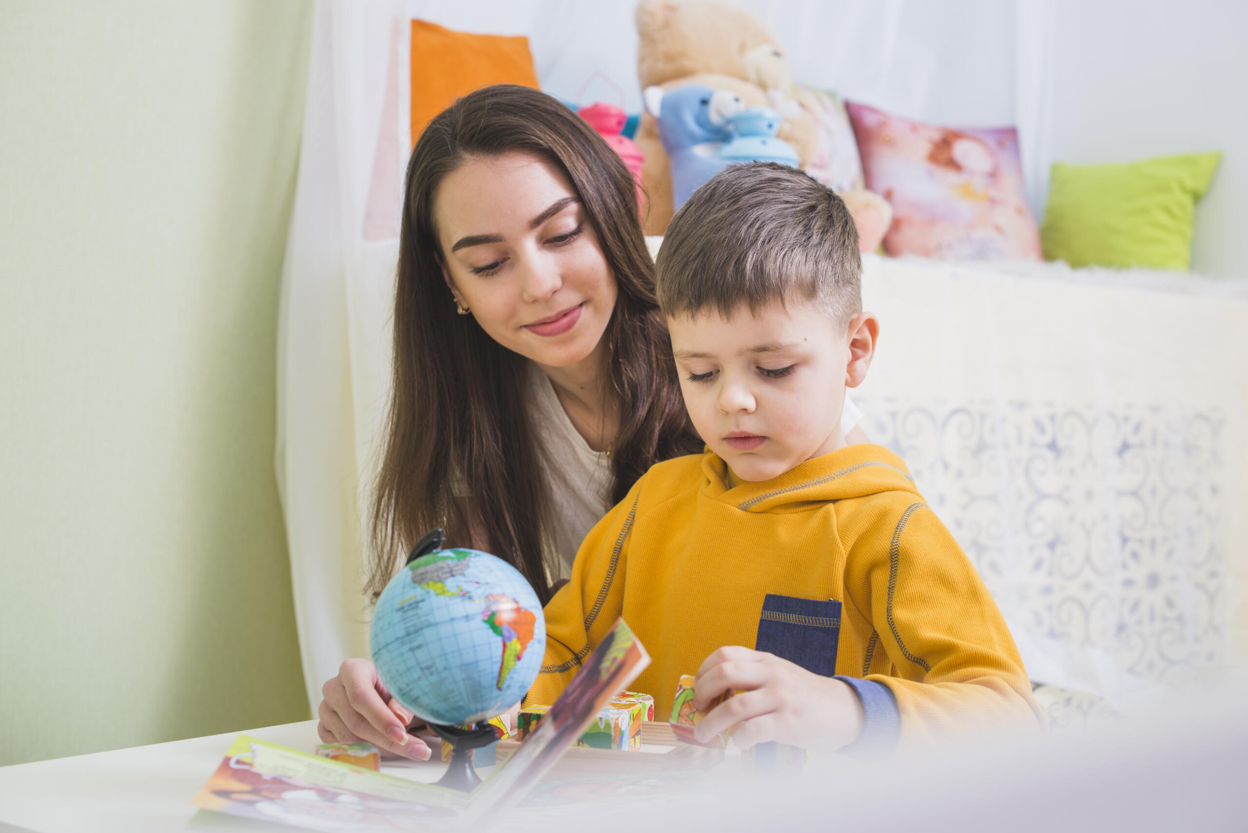maestra sentada junto a un niño en un escritorio con un cuaderno y globo terráqueo sobre la mesa