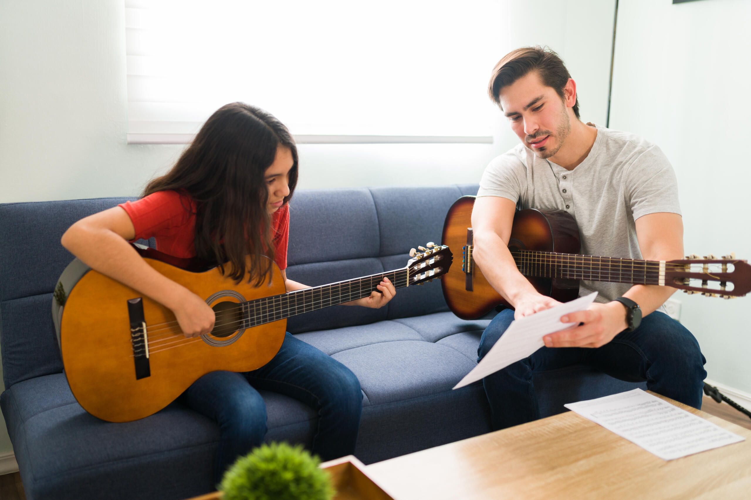 profesor enseñándole notas musicales a su alumna, ambos con una guitarra