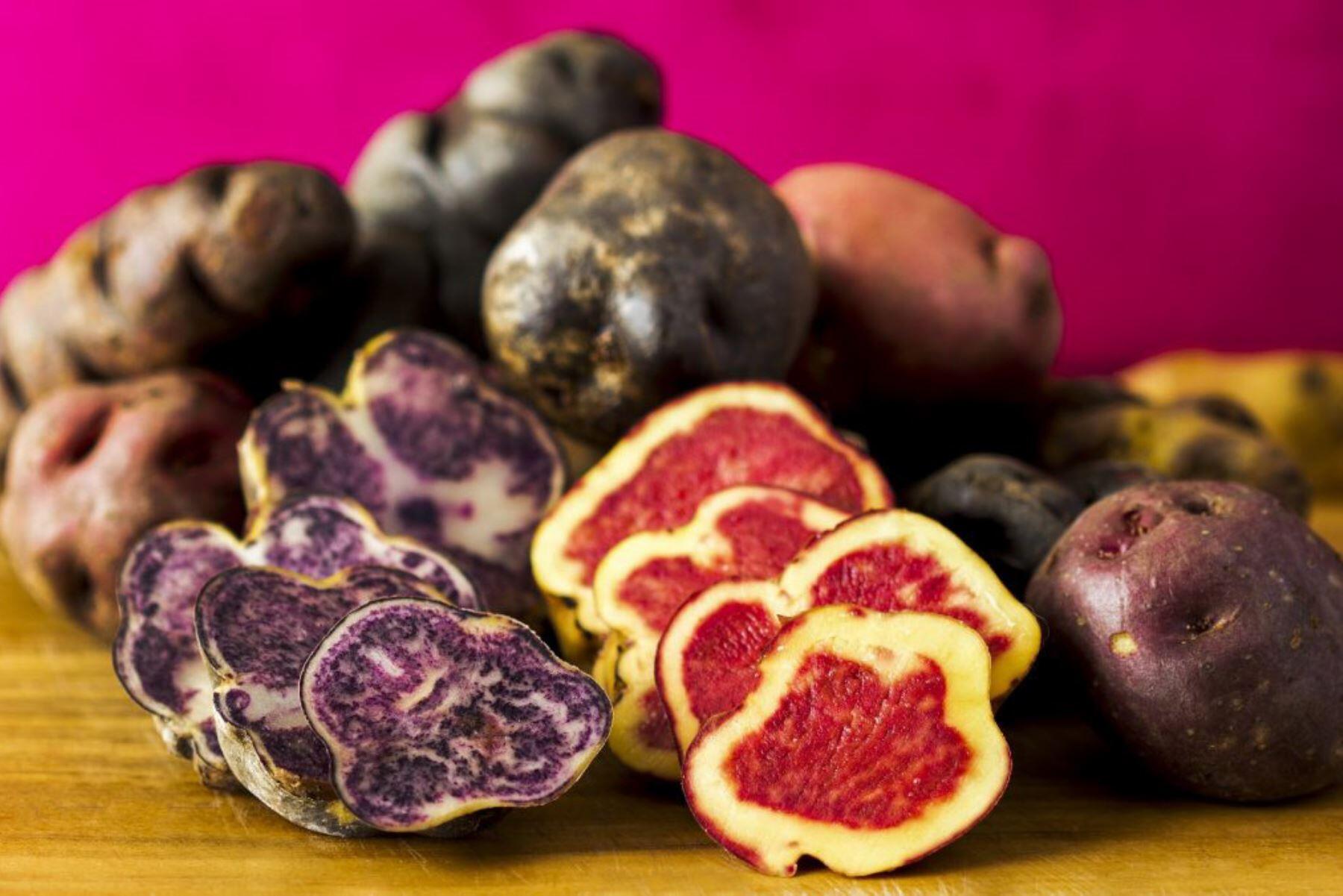 vista de papas nativas apiladas y dos de ellas cortadas a la mitad con interior rojo y morado