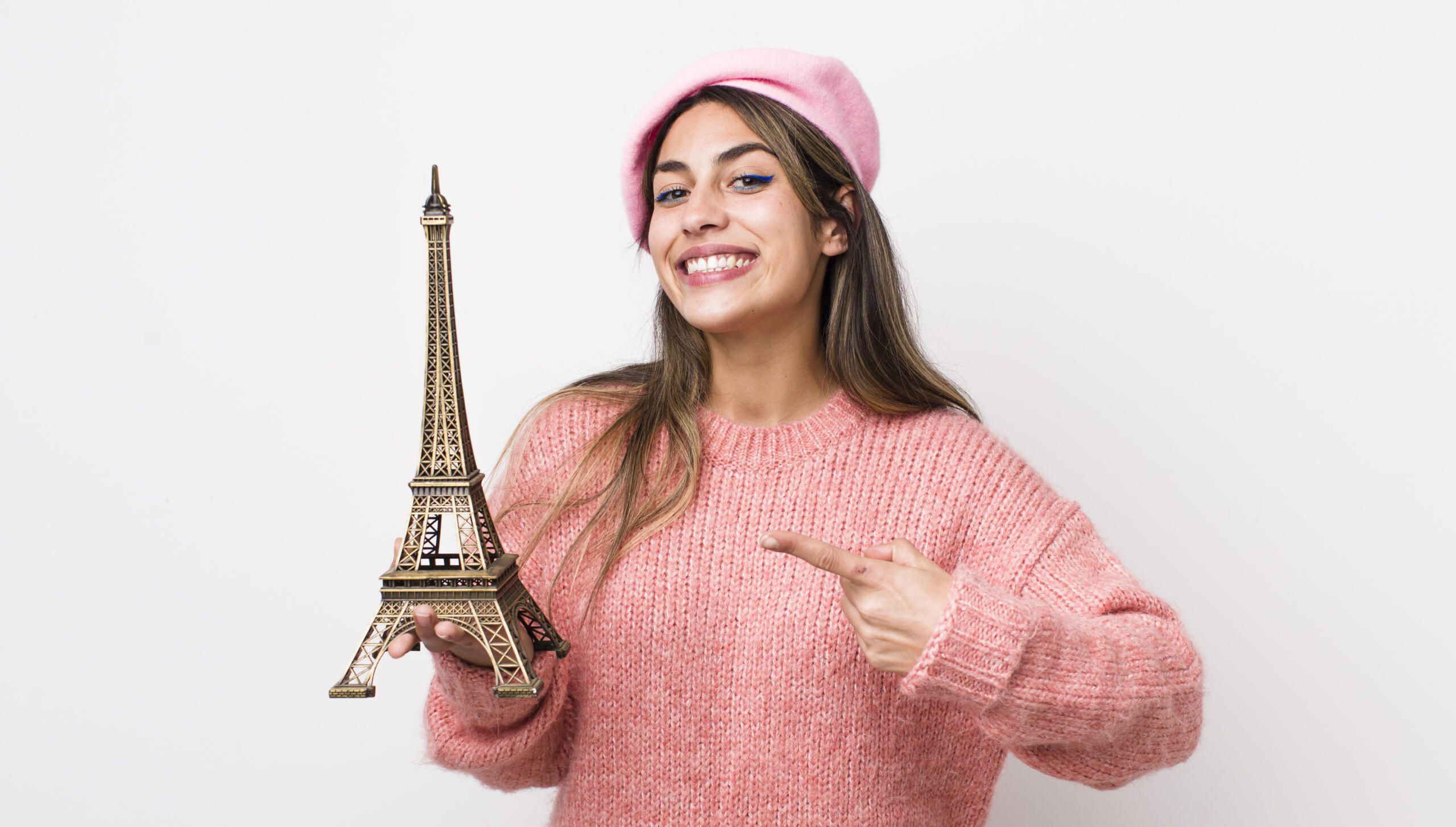chica sonriente con una boina y chompa rosa sosteniendo la torre eiffel.