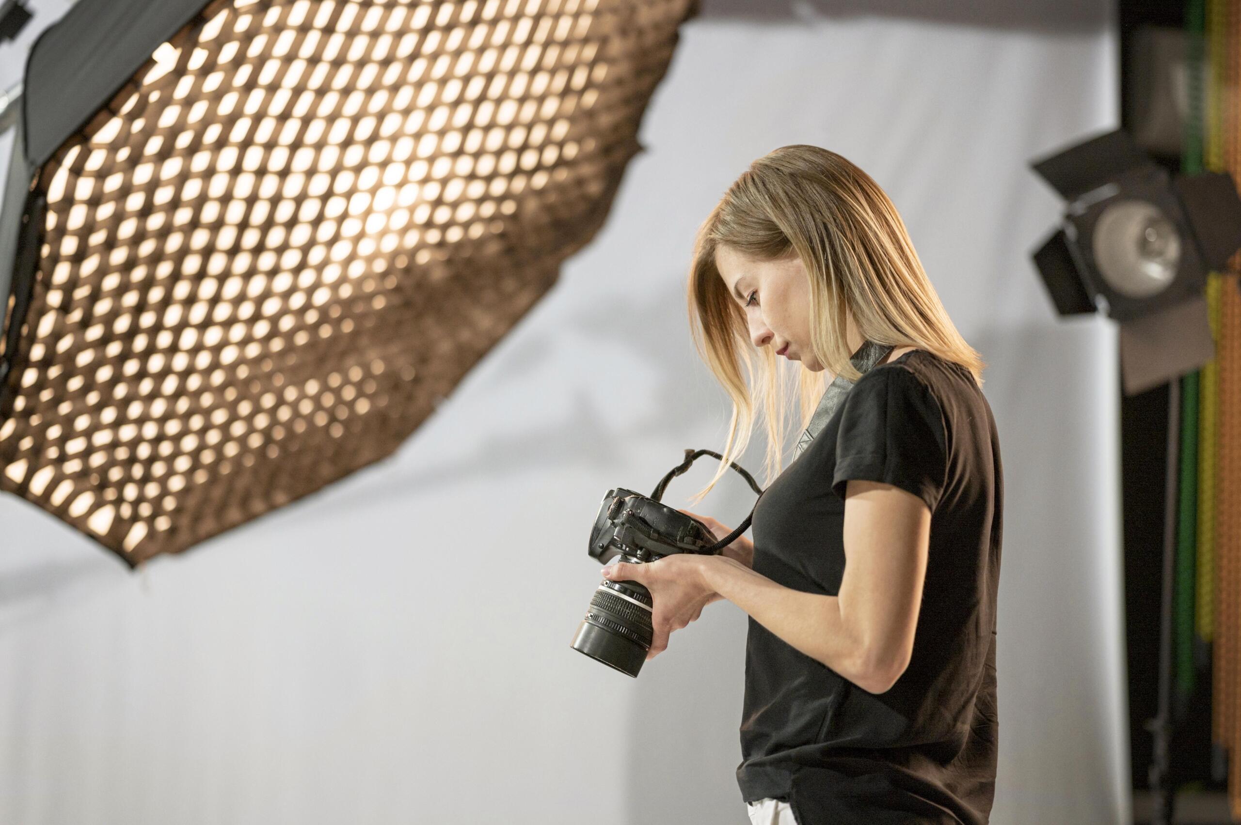 chica de perfil mirando su cámara en manos en medio de un estudio fotográfico